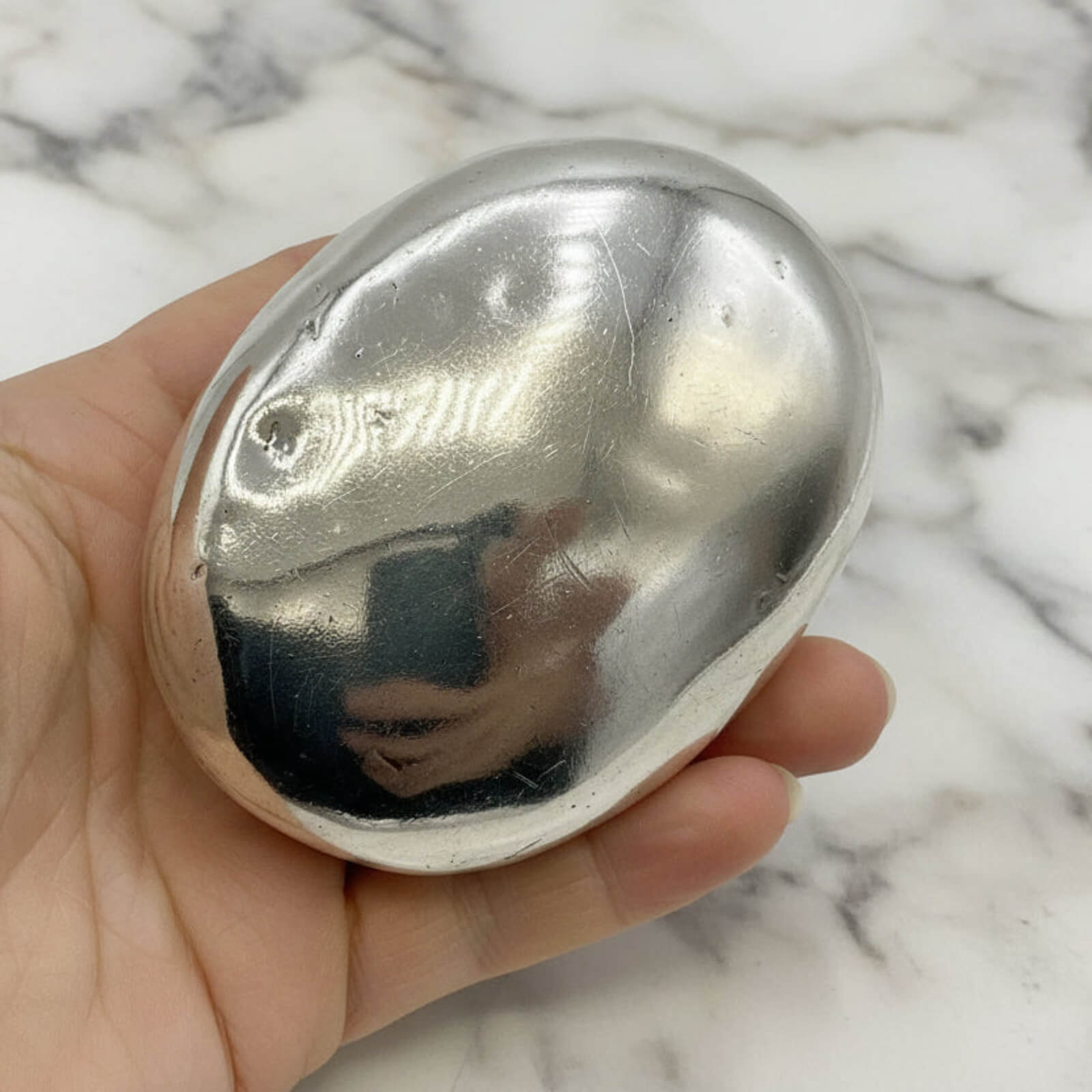 base of silver box held in a hand against a marble background