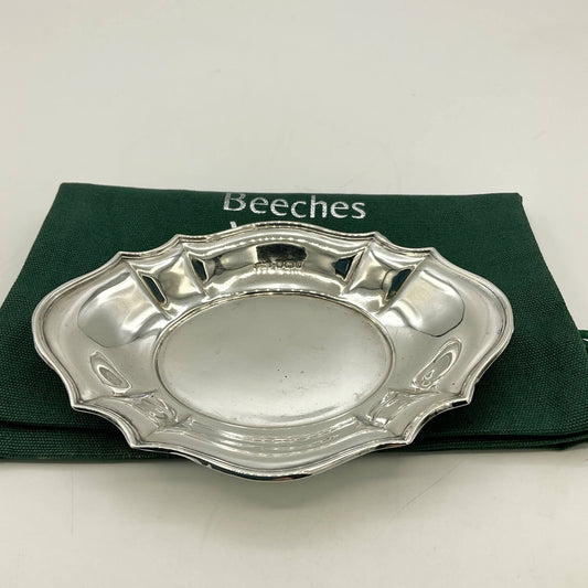 A polished silver oval serving tray with decorative scalloped edges, displayed on a dark green Beeches Vintage cloth bag against a plain white background.