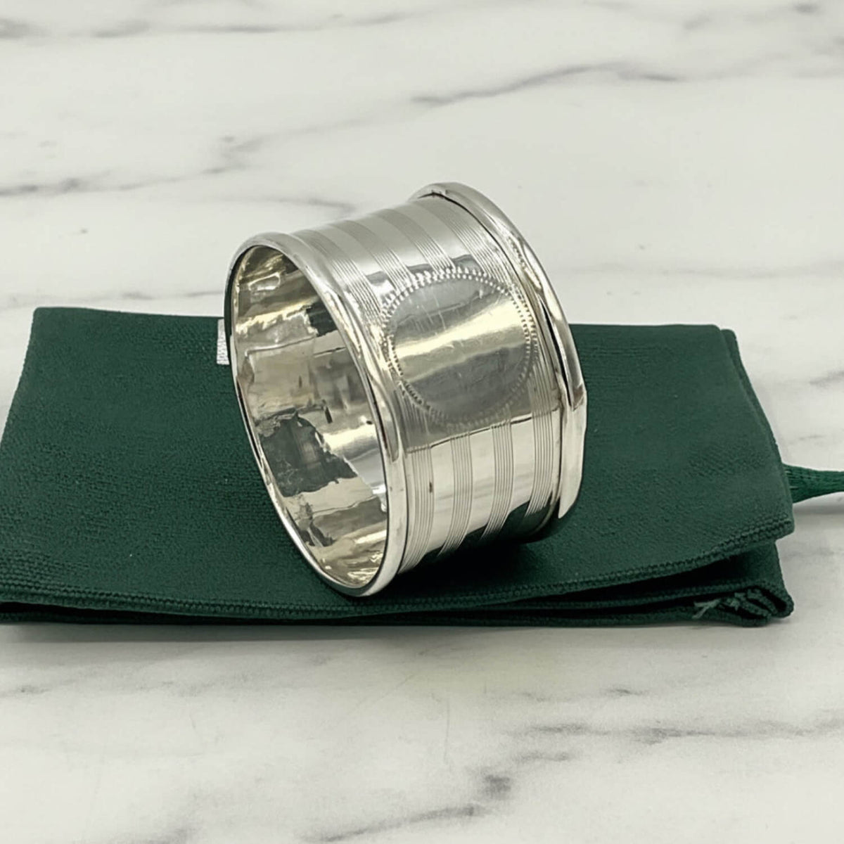 Antique 1920 Sterling Silver Napkin ring with horizontal ridges, resting on a folded dark green fabric pouch against a plain white background.