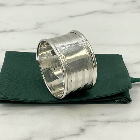 Antique 1920 Sterling Silver Napkin ring with horizontal ridges, resting on a folded dark green fabric pouch against a plain white background.