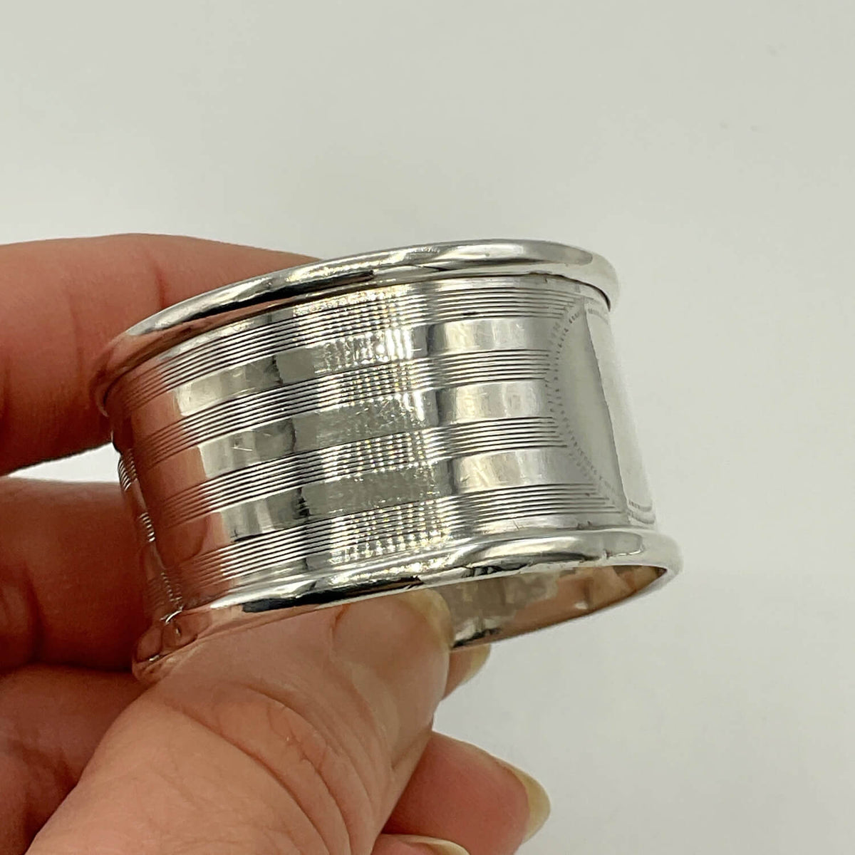 Antique 1920 Sterling Silver Napkin ring with horizontal grooved lines, held in a person's hand against a plain light background.