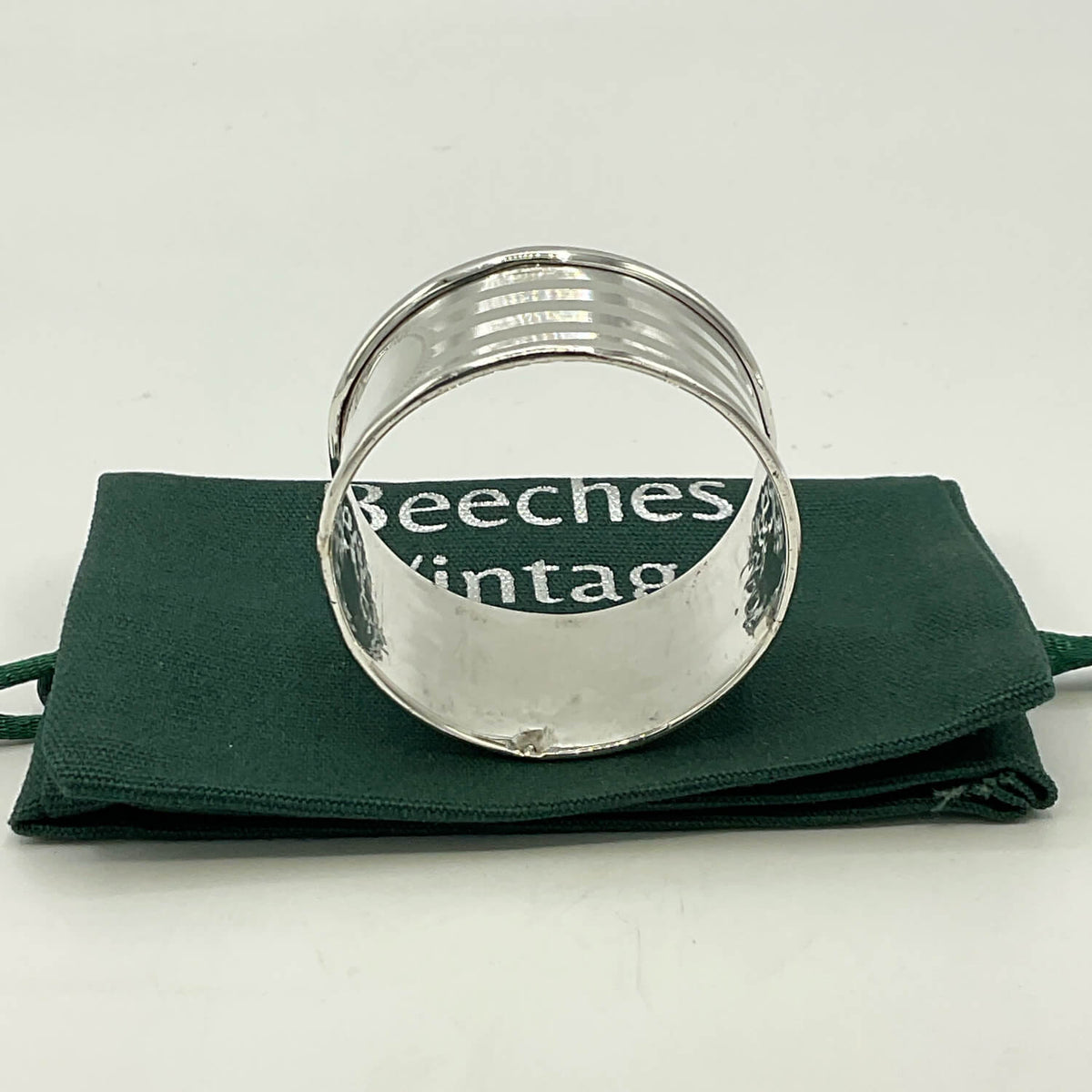 Antique 1920 Sterling Silver Napkin ring resting on a dark green fabric pouch with white text that reads 'Beeches Vintage'.