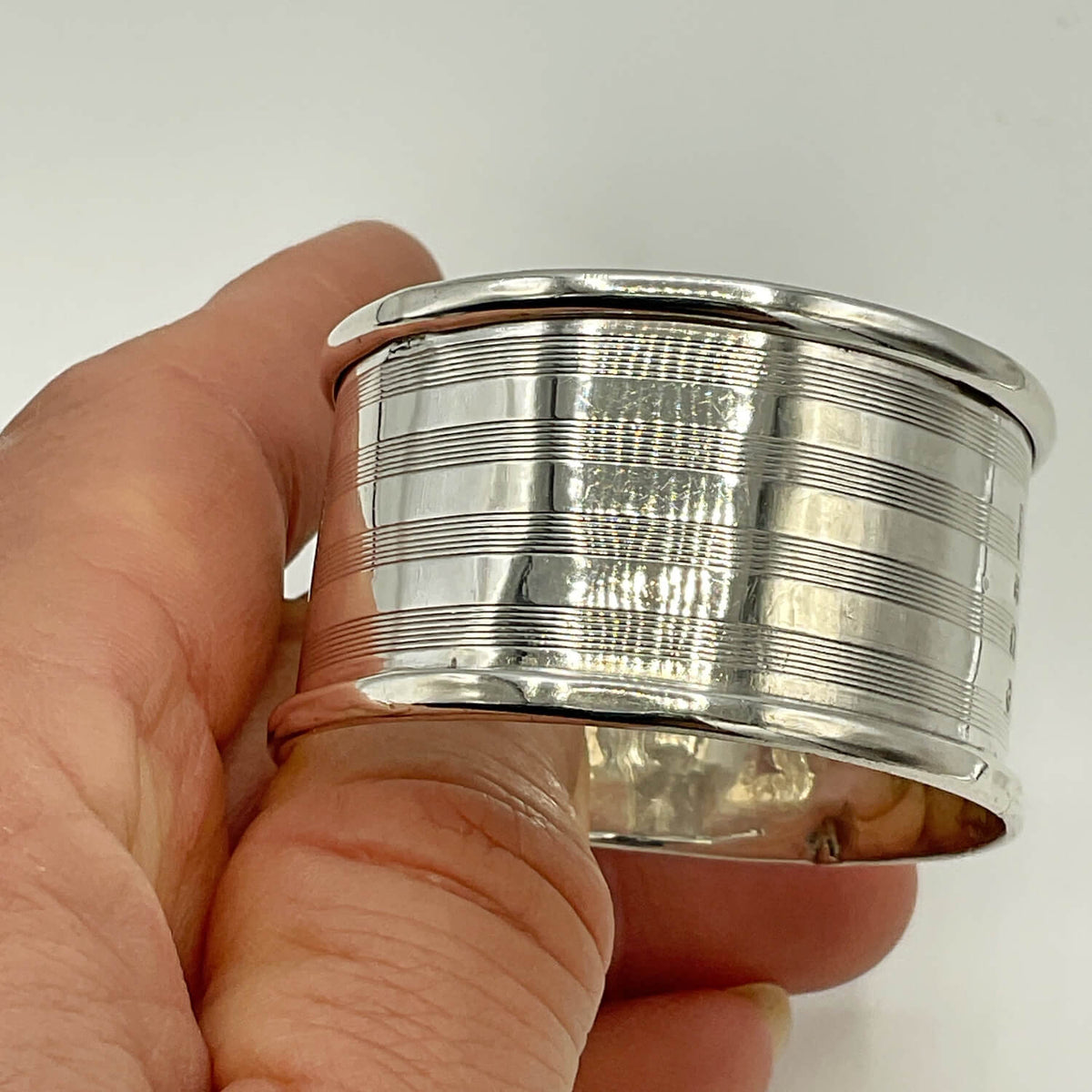 A polished Antique 1920 Sterling Silver Napkin ring with horizontal grooved detailing, held in a person's hand against a plain white background.