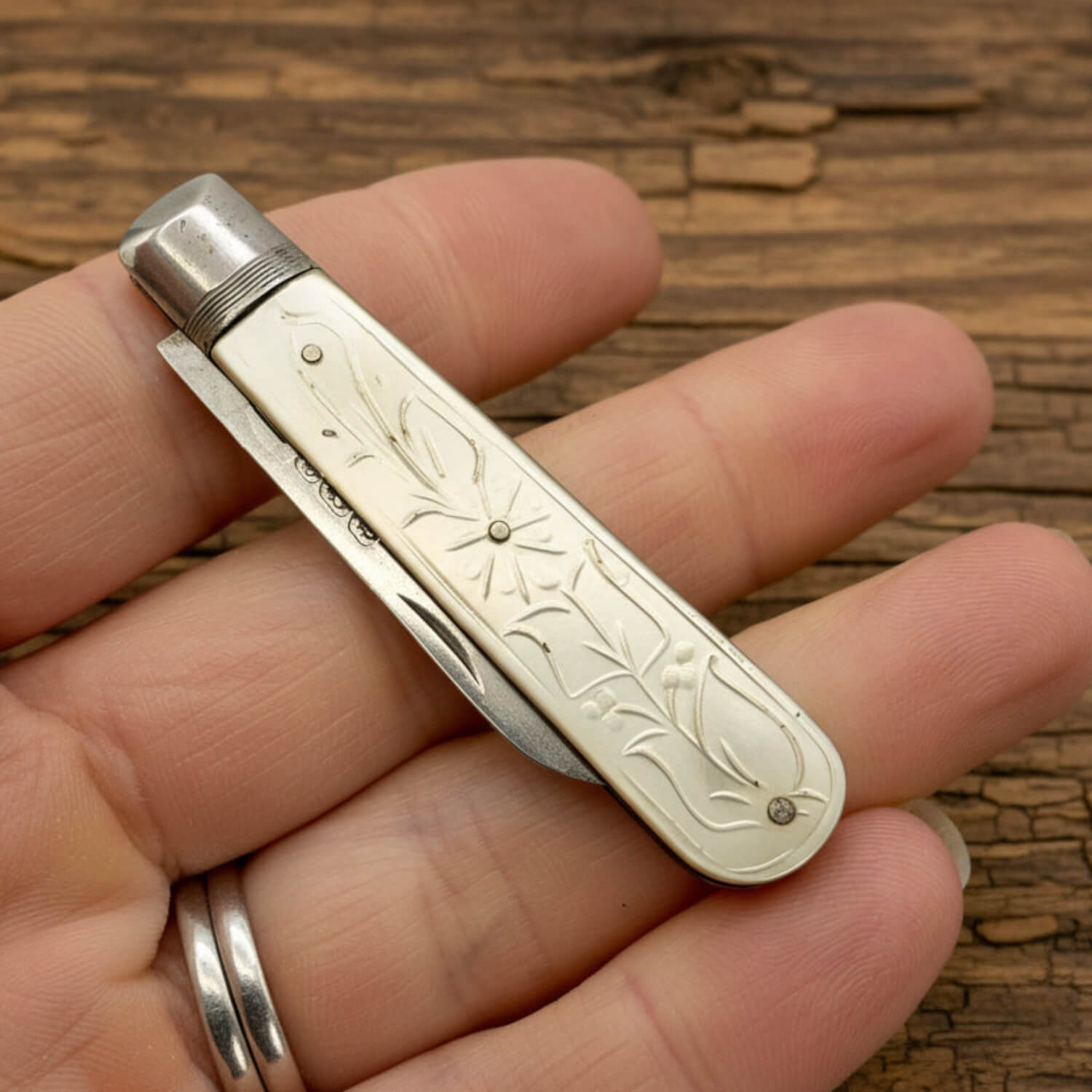 Hand holding a decorative fruit knife with intricate engravings on a wooden surface