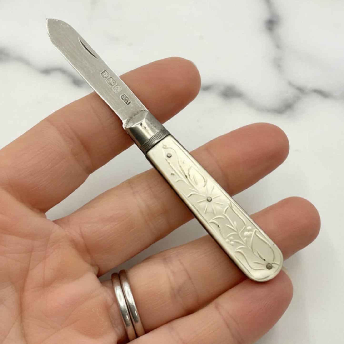 Small fruit knife with decorative handle held in a hand against a marble background