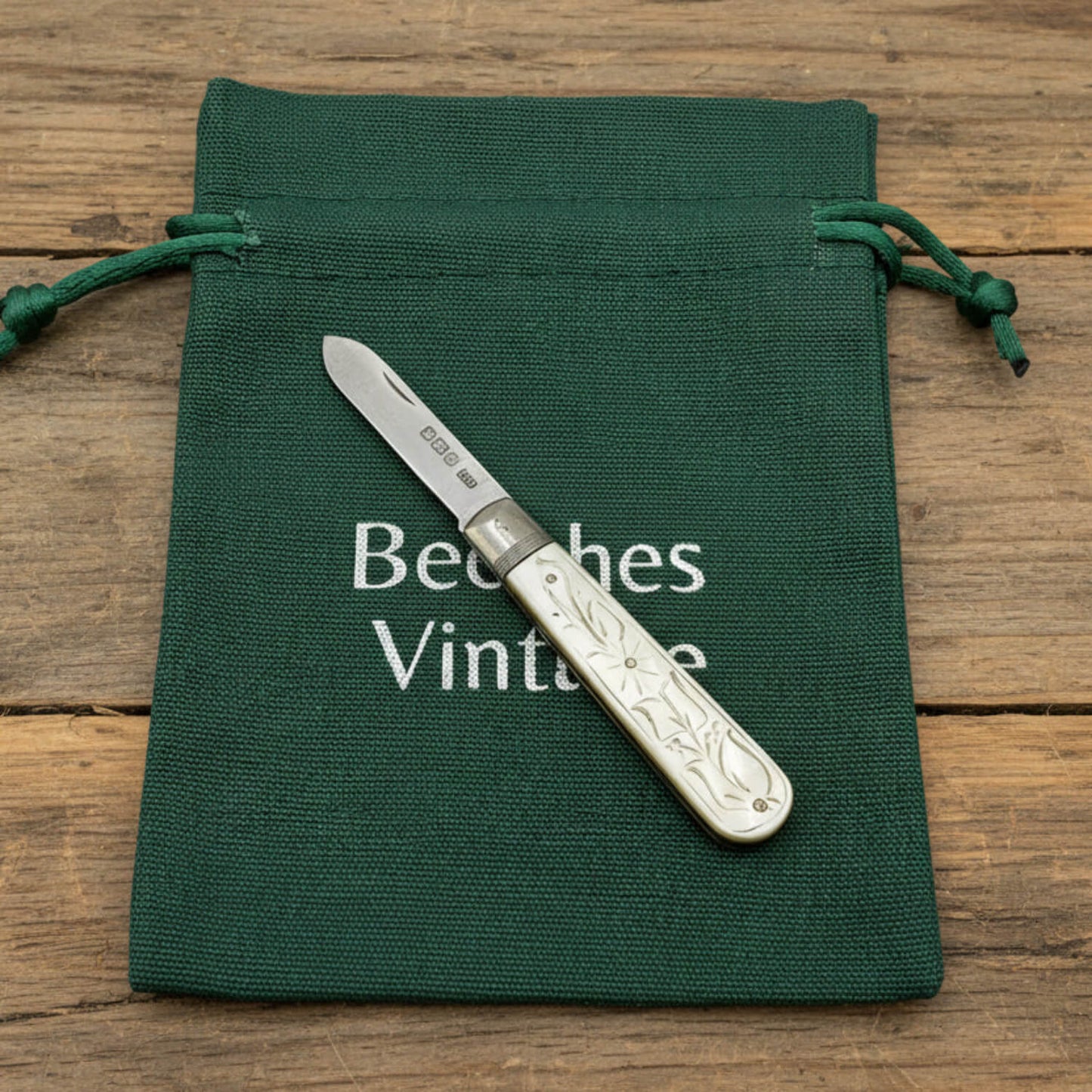 Silver fruit knife on a green drawstring bag with 'Beeches Vintage' text on a wooden surface