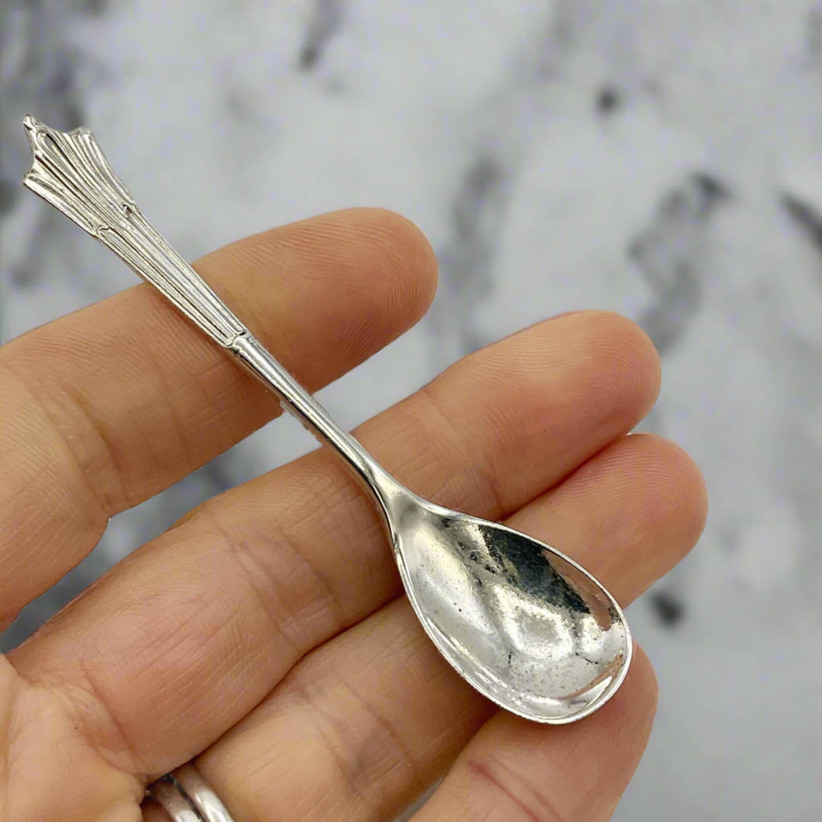 Silver spoon held in a hand against a marble background