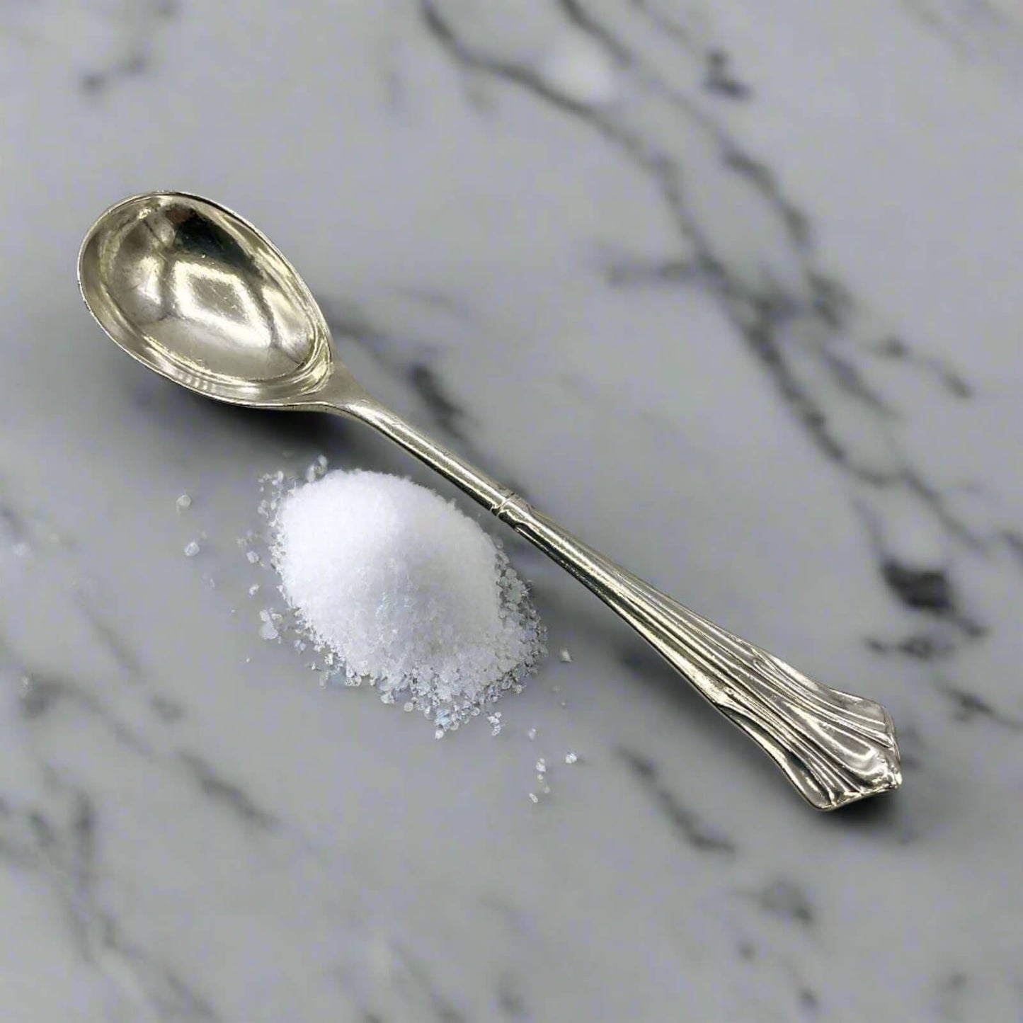 Silver spoon with a small pile of salt on a marble surface