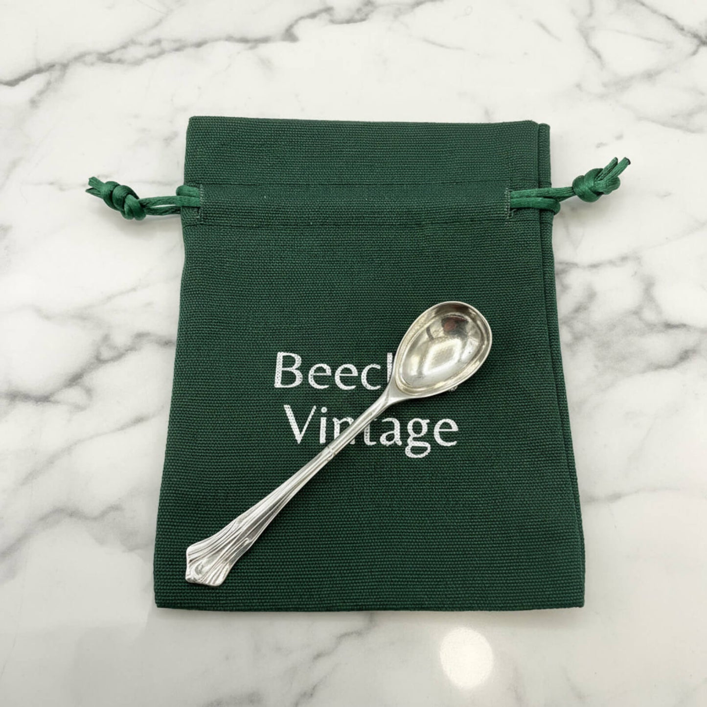 Silver spoon on a green drawstring bag with 'Beech Vintage' text on a marble background