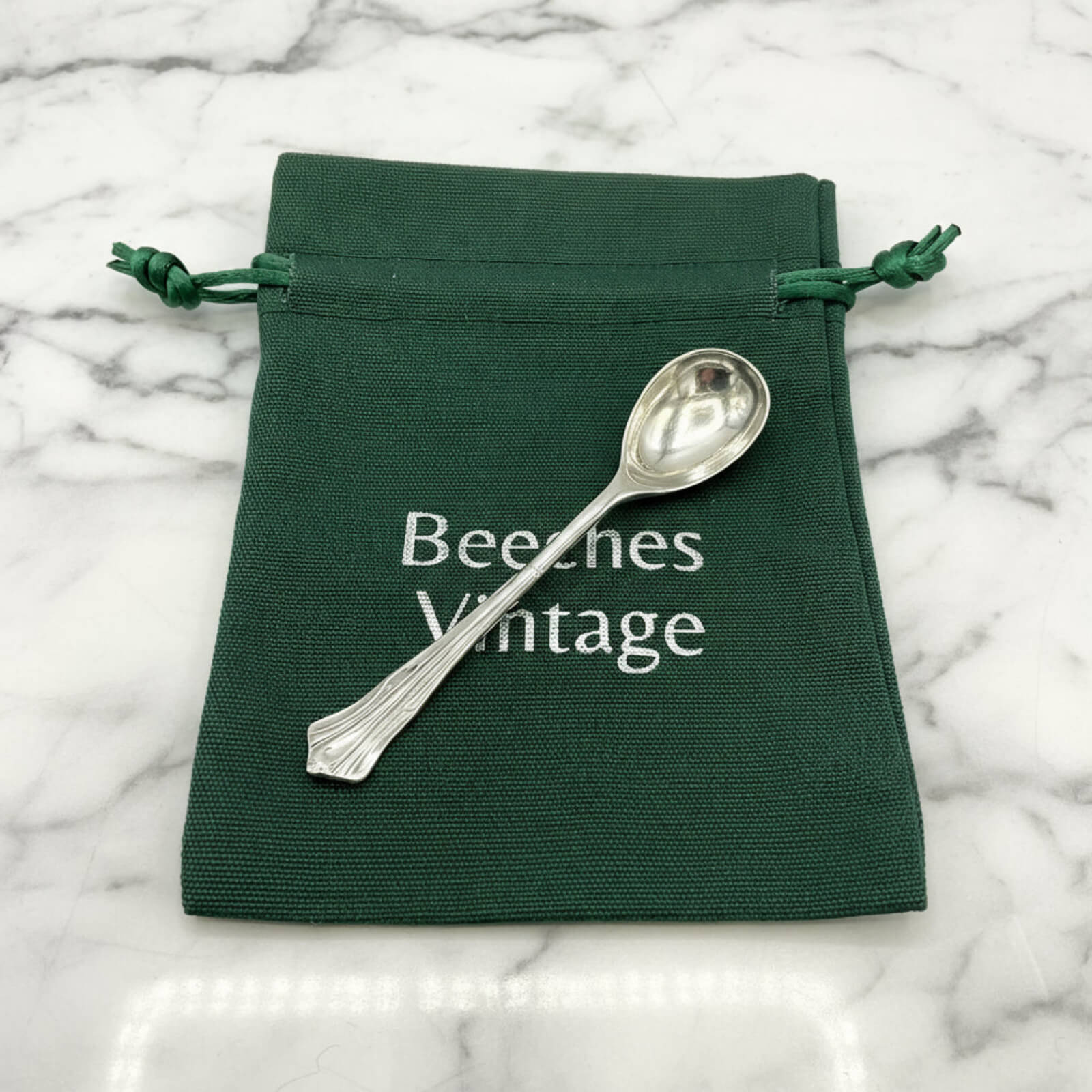 Antique Art Deco Sterling Silver Salt Spoon on a green bag on marble surface