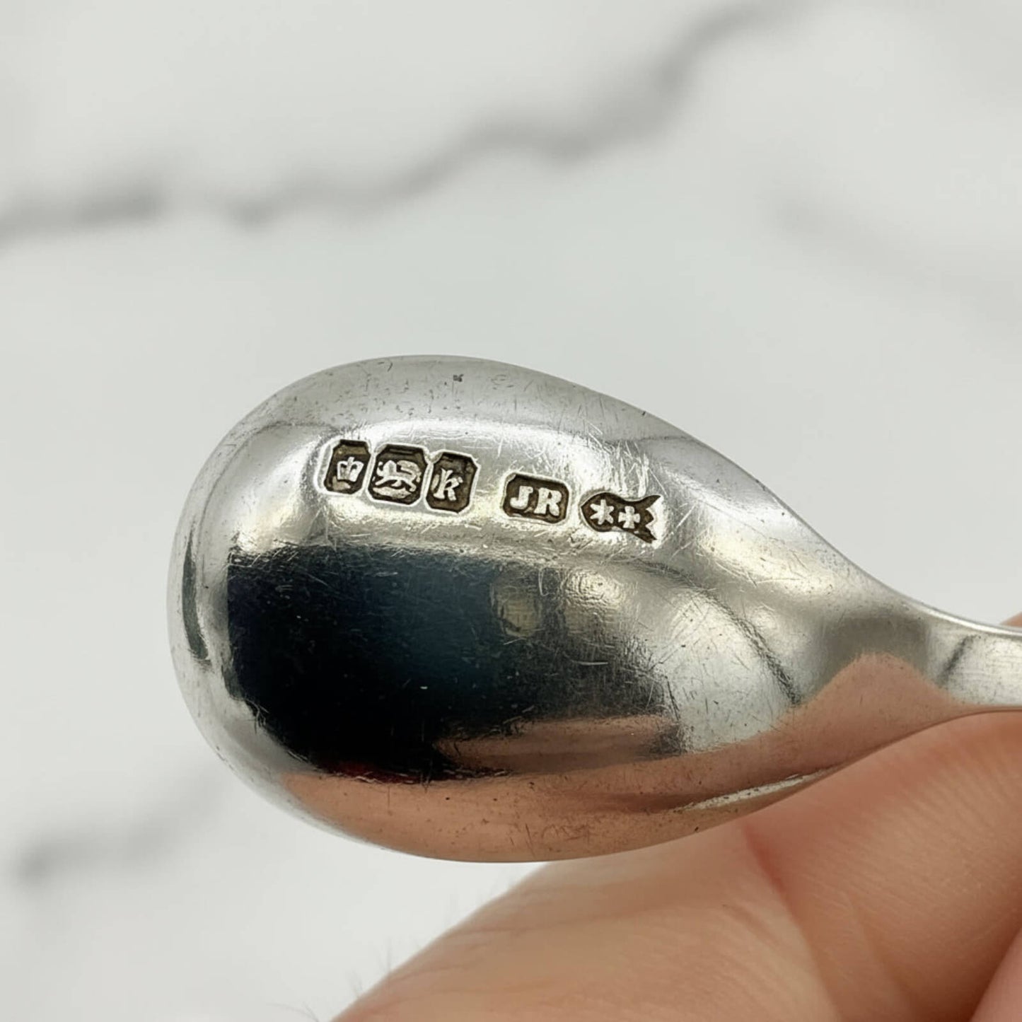 Silver spoon held by a hand with visible hallmarks on a light background