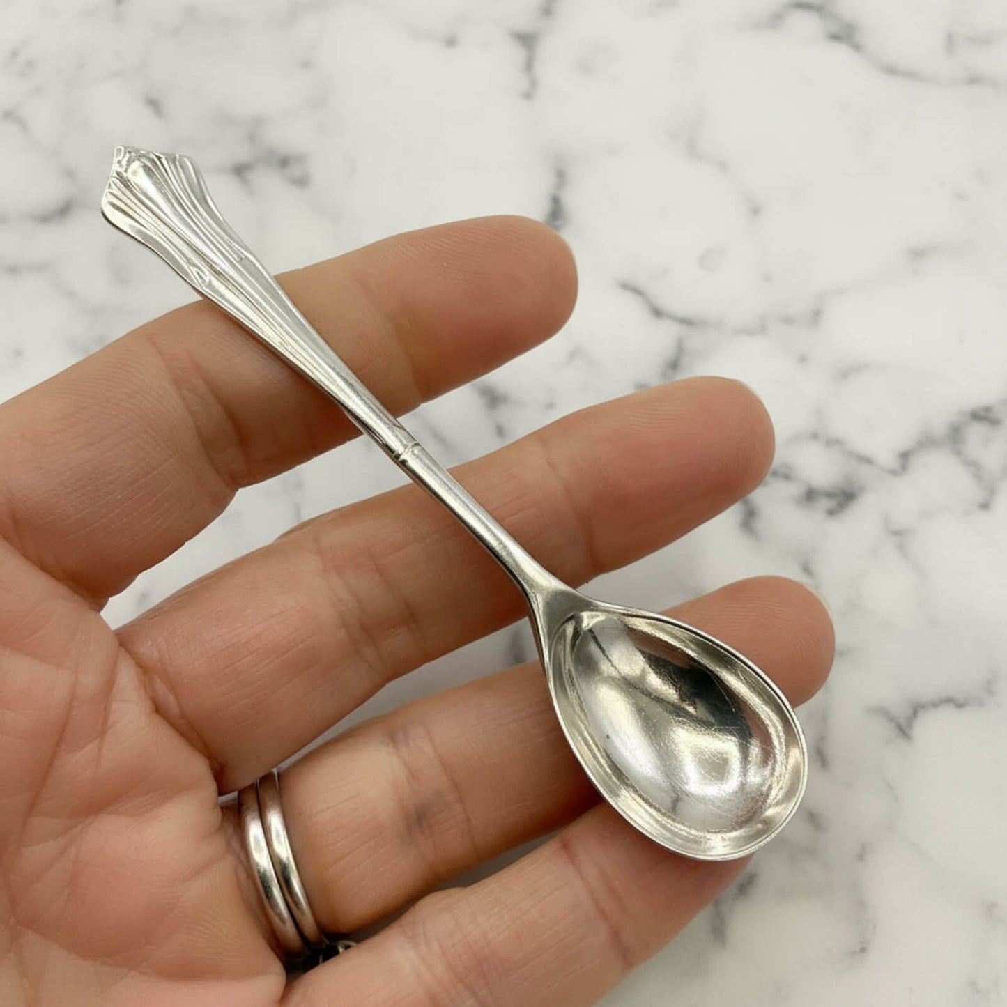 Silver spoon held in a hand against a marble background