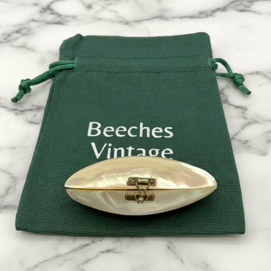 Shell-shaped pill box on a green drawstring bag with 'Beeches Vintage' text on a marble background