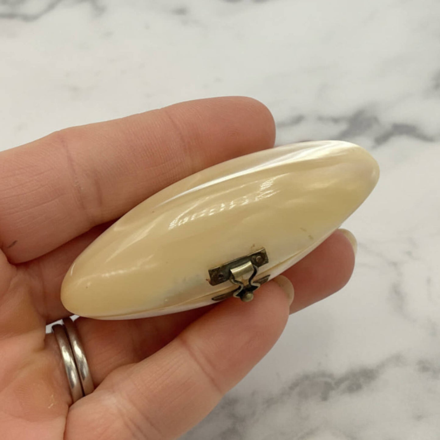 Hand holding a small, oval-shaped shell box against a marble background