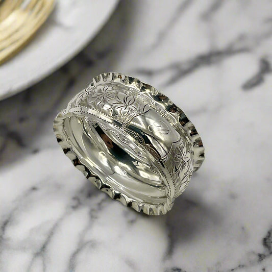 Silver ring with intricate designs on a marble background with a plate next to it