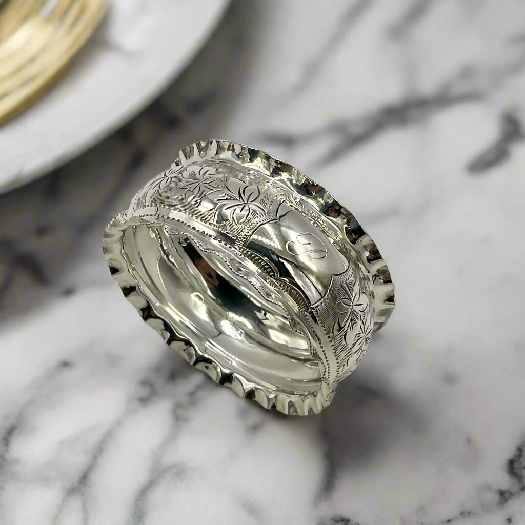 Silver ring with intricate designs on a marble background with a plate next to it