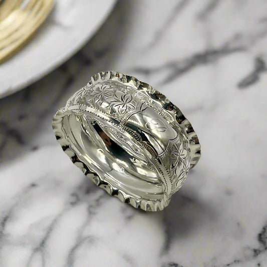 Silver ring with intricate designs on a marble background with a plate next to it