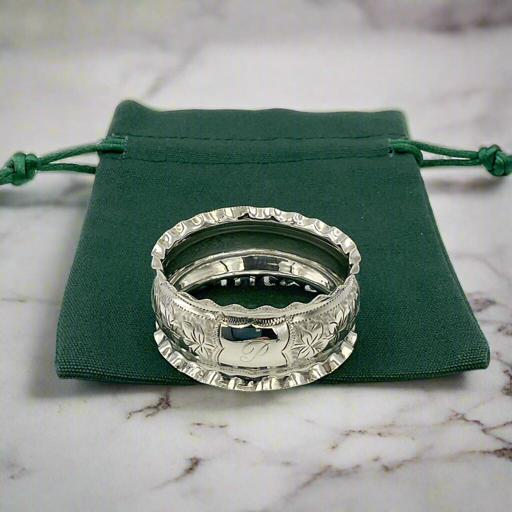 Silver ring with intricate design on a green drawstring bag on a marble worktop