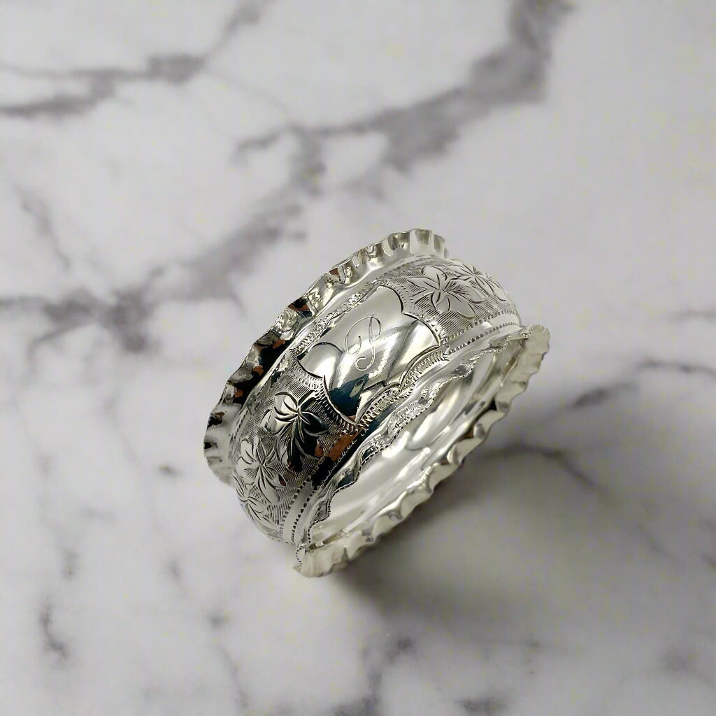 Silver napkin ring with intricate engravings on a light marble background 