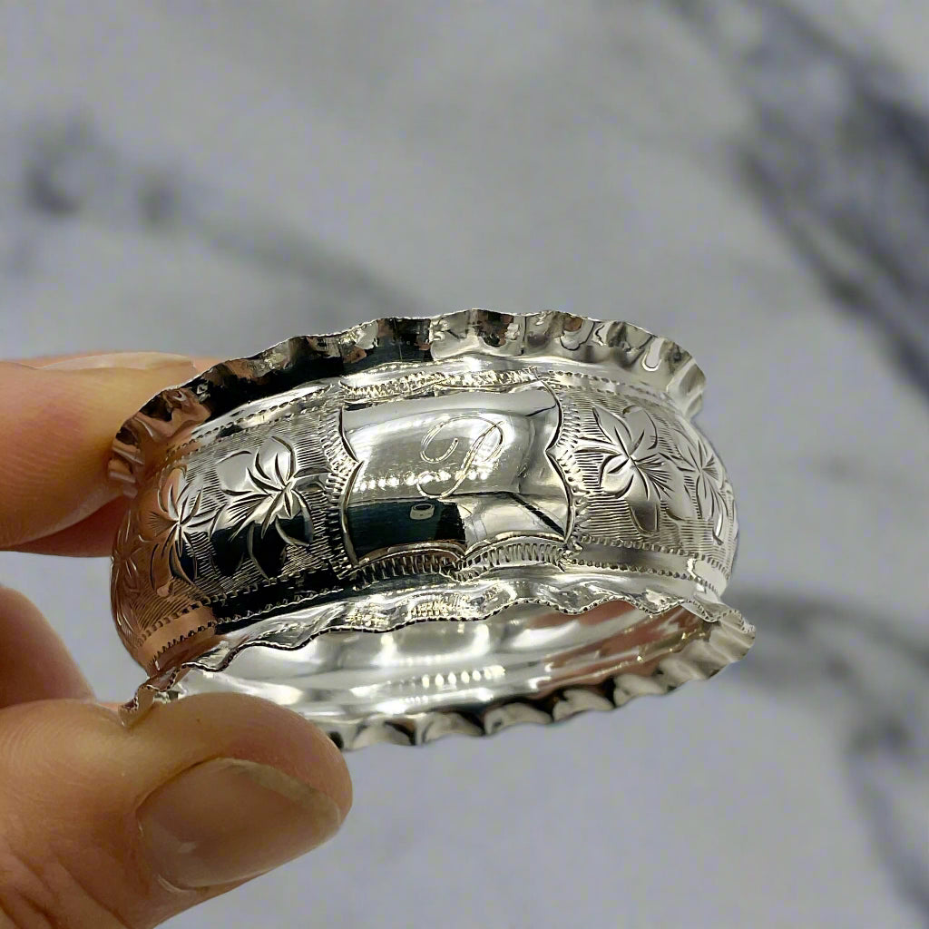 Silver napkin ring with intricate designs held by a hand on a marble background 