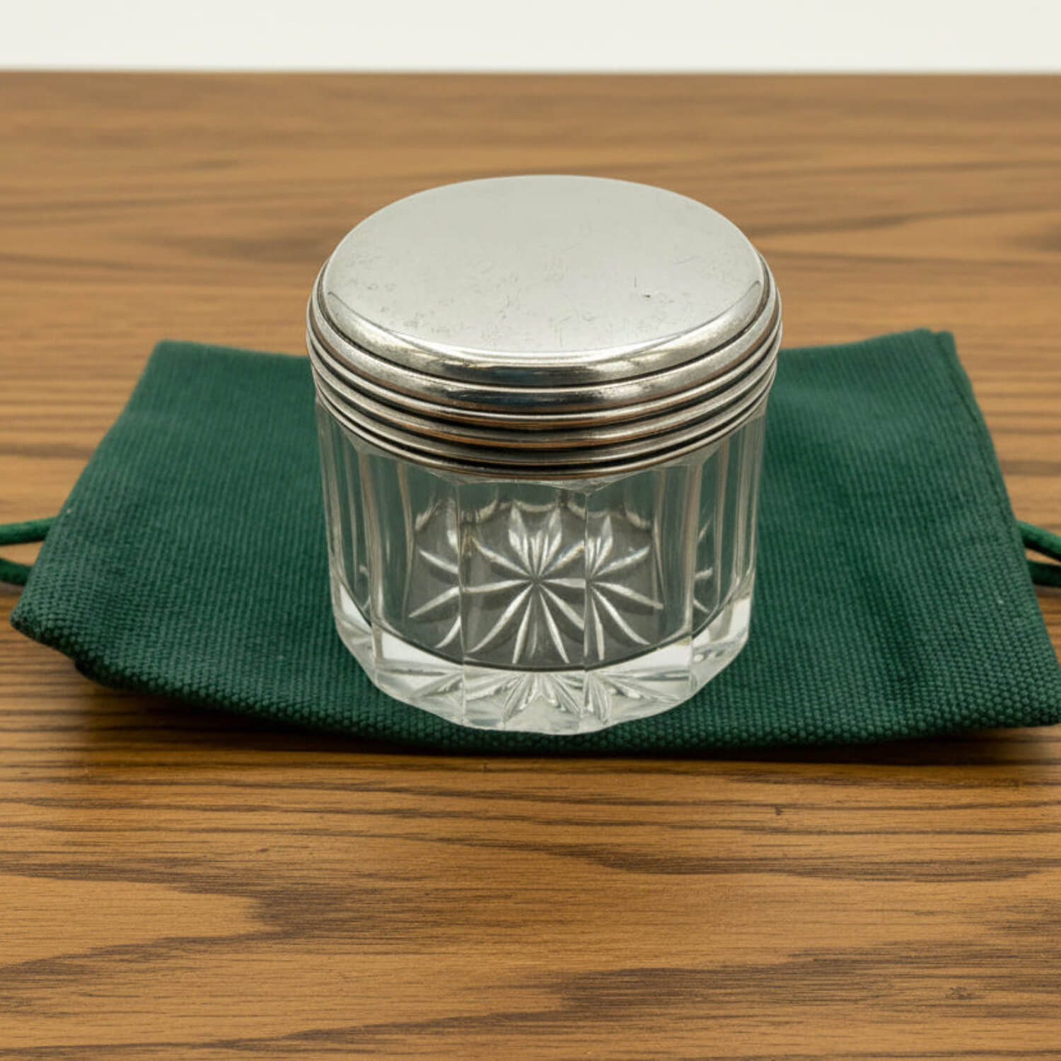 Decorative glass jar with silver lid on a green cloth over a wooden surface