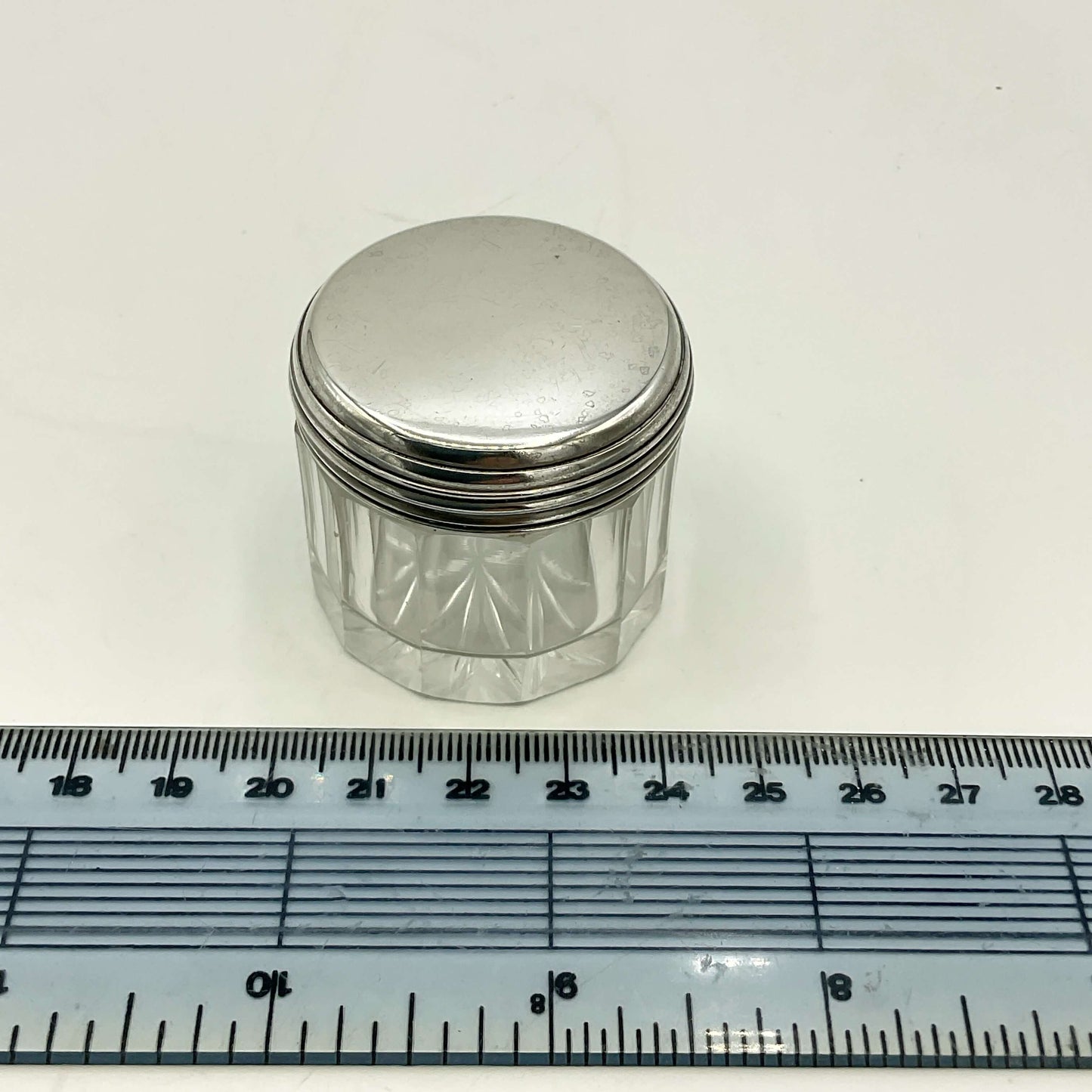 Small glass jar with a silver lid next to a ruler on a white background