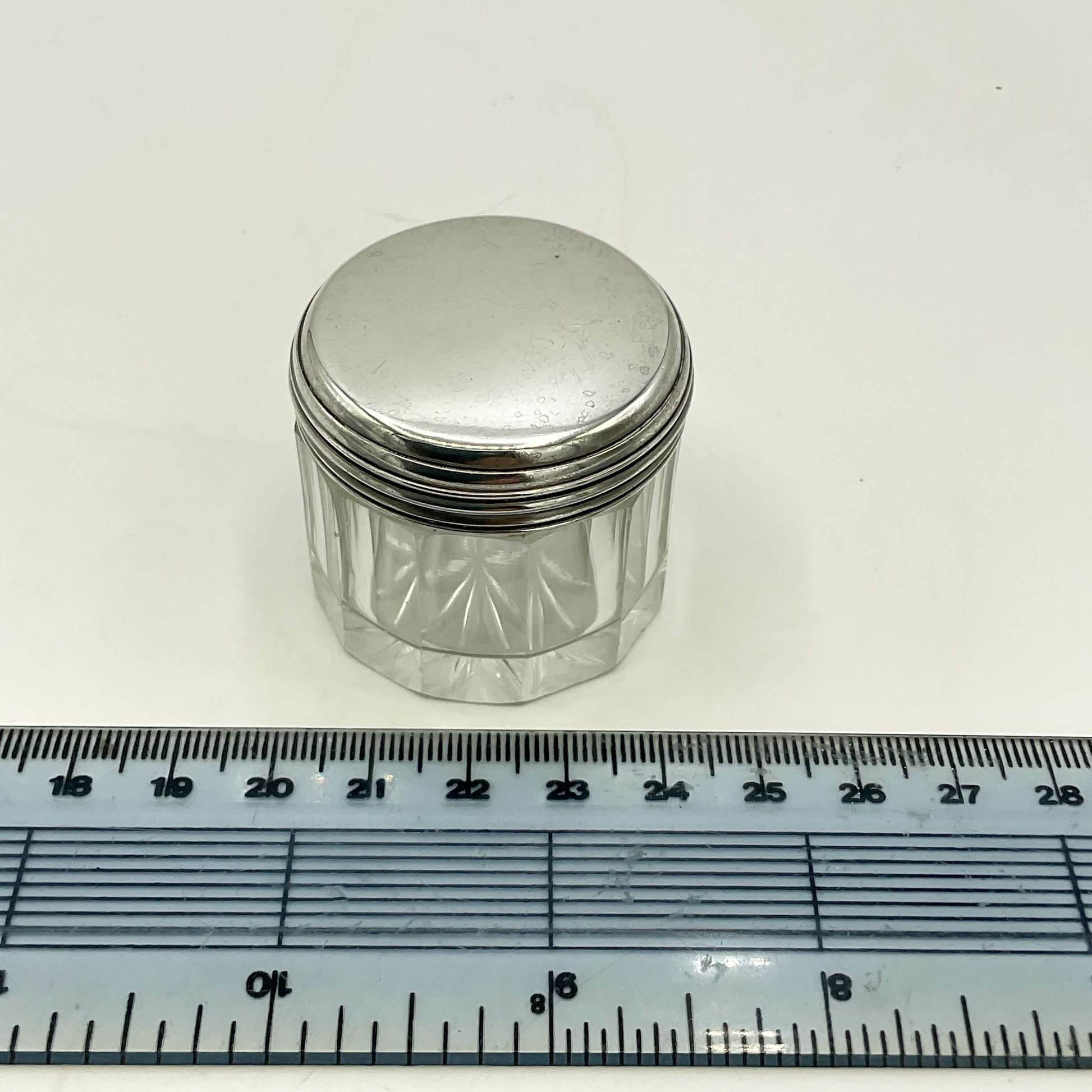 Small glass jar with a silver lid next to a ruler on a white background