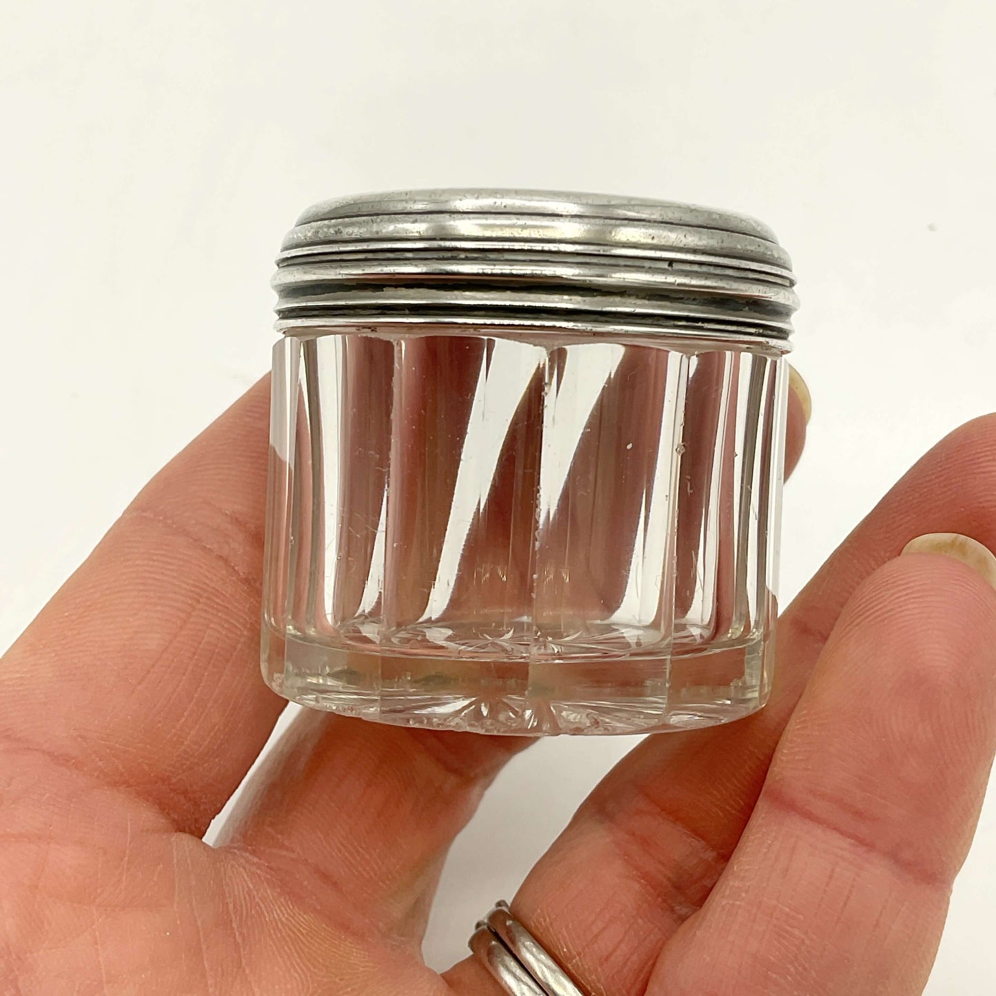 Small glass jar with a silver lid held in a hand against a white background