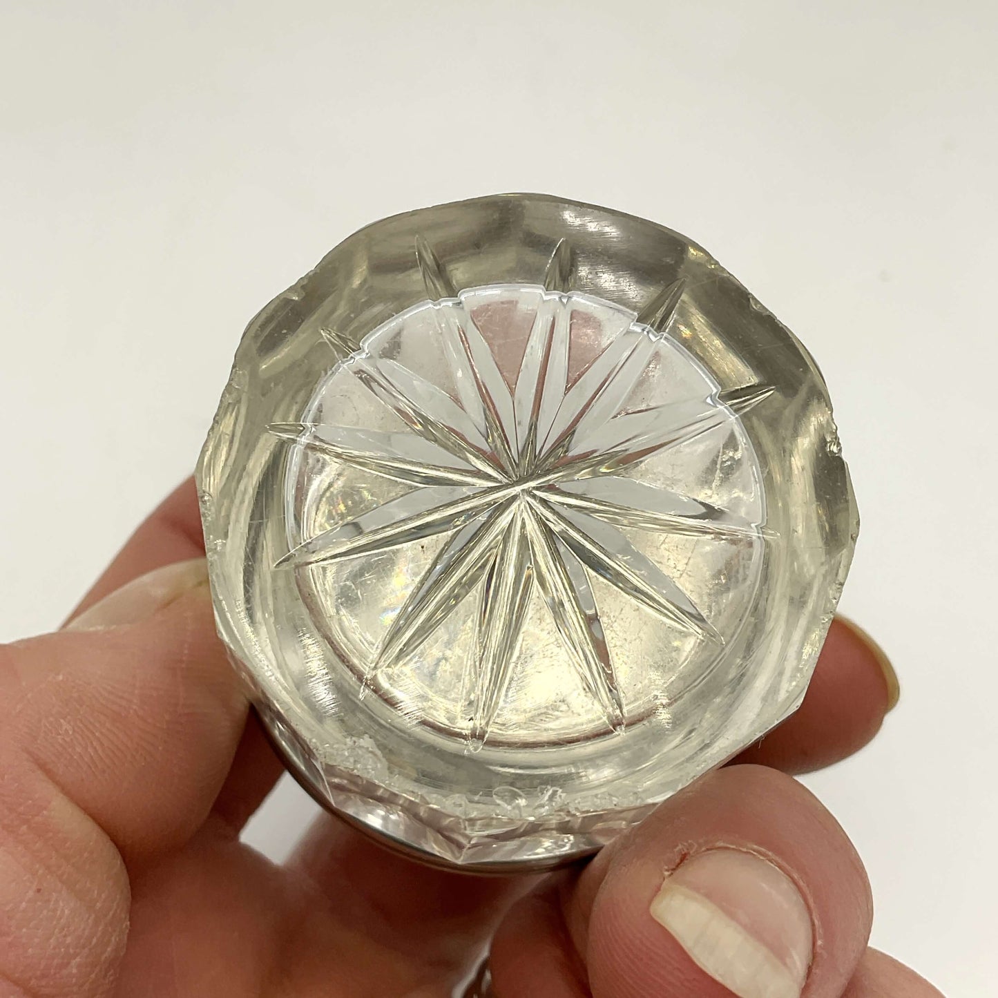 Clear glass base of silver lidded glass jar held in a hand against a white background