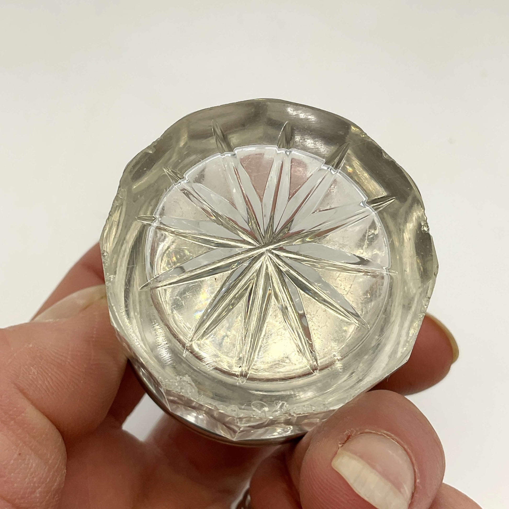 Clear glass base of silver lidded glass jar held in a hand against a white background