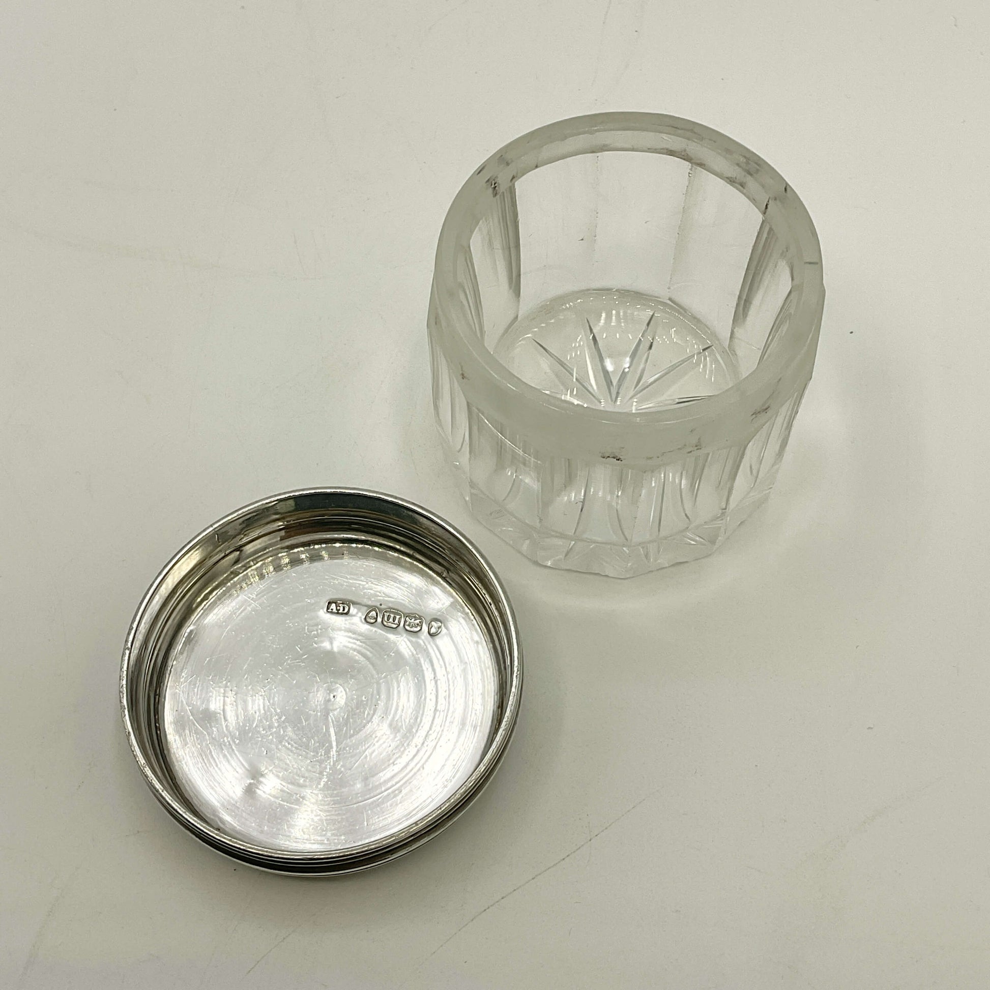Clear glass jar with silver lid upside down showing hallmarks on a light grey background