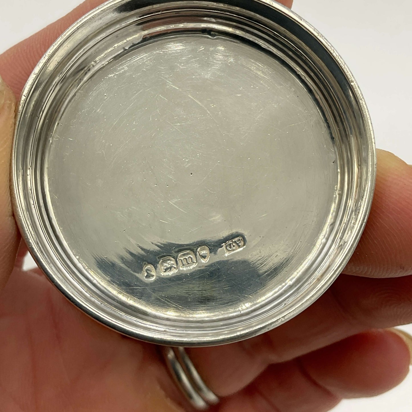 Close-up of a silver lid showing hallmarks held in a hand with a white background