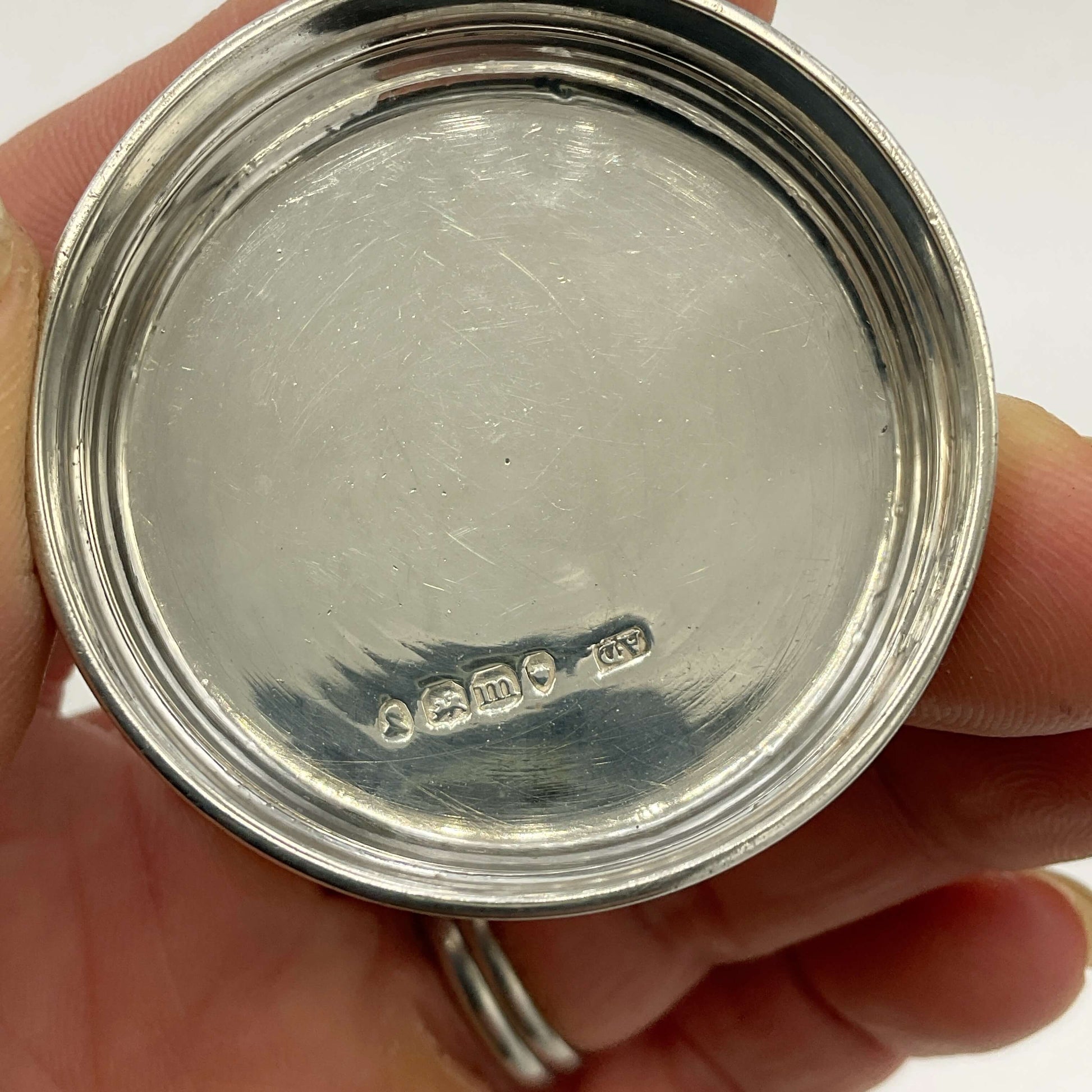 Close-up of a silver lid showing hallmarks held in a hand with a white background