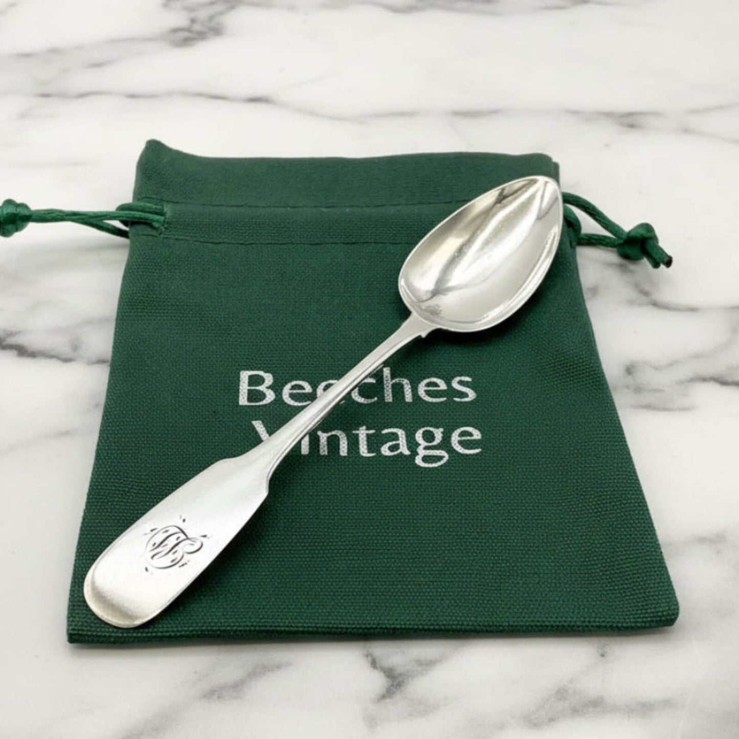 Silver spoon on a green 'Beeches Vintage' pouch against a marble background