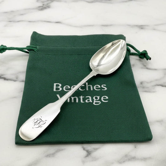 Silver spoon on a green 'Beeches Vintage' pouch against a marble background