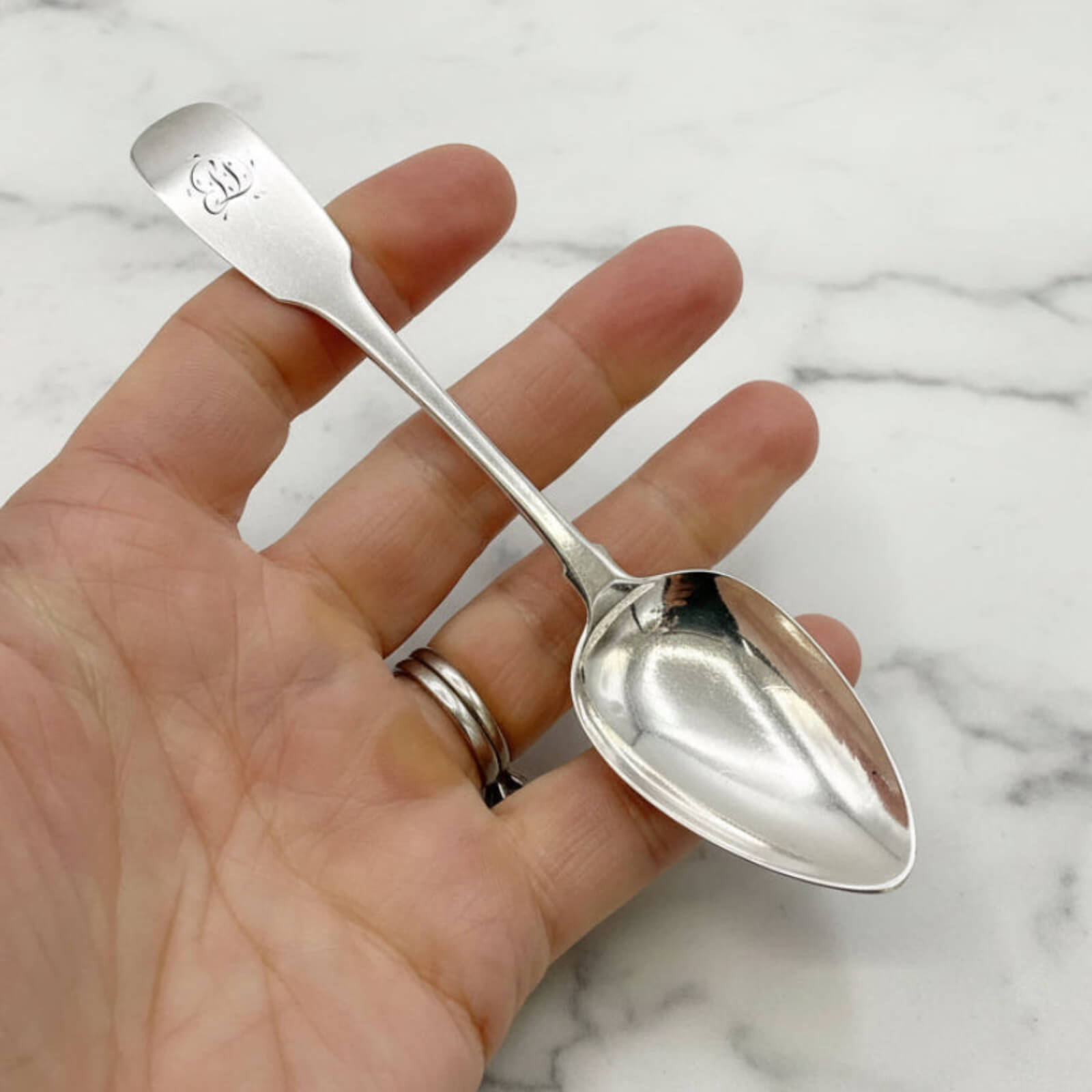 Silver spoon held in a hand against a marble background