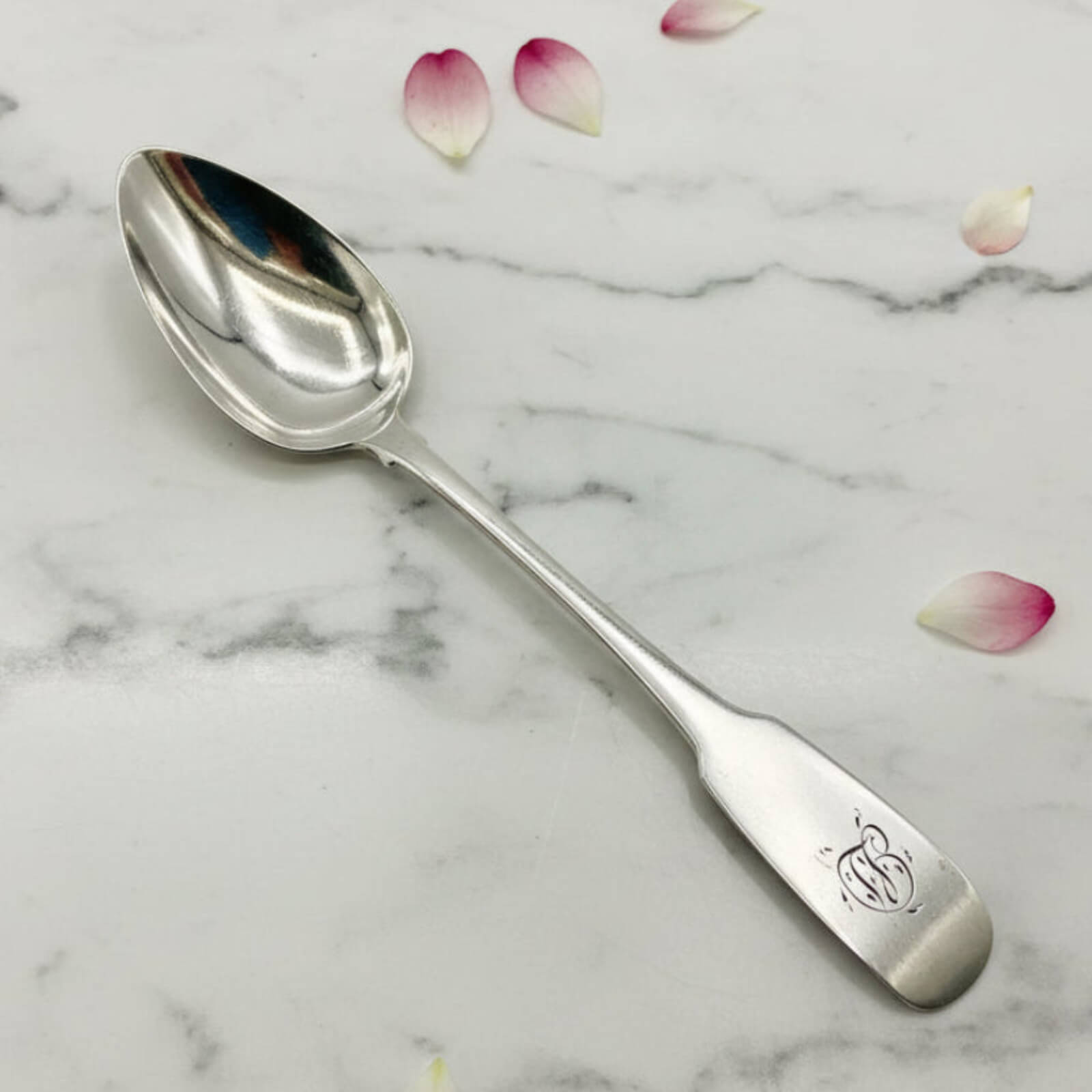 Silver spoon with engraved design on a marble surface with flower petals