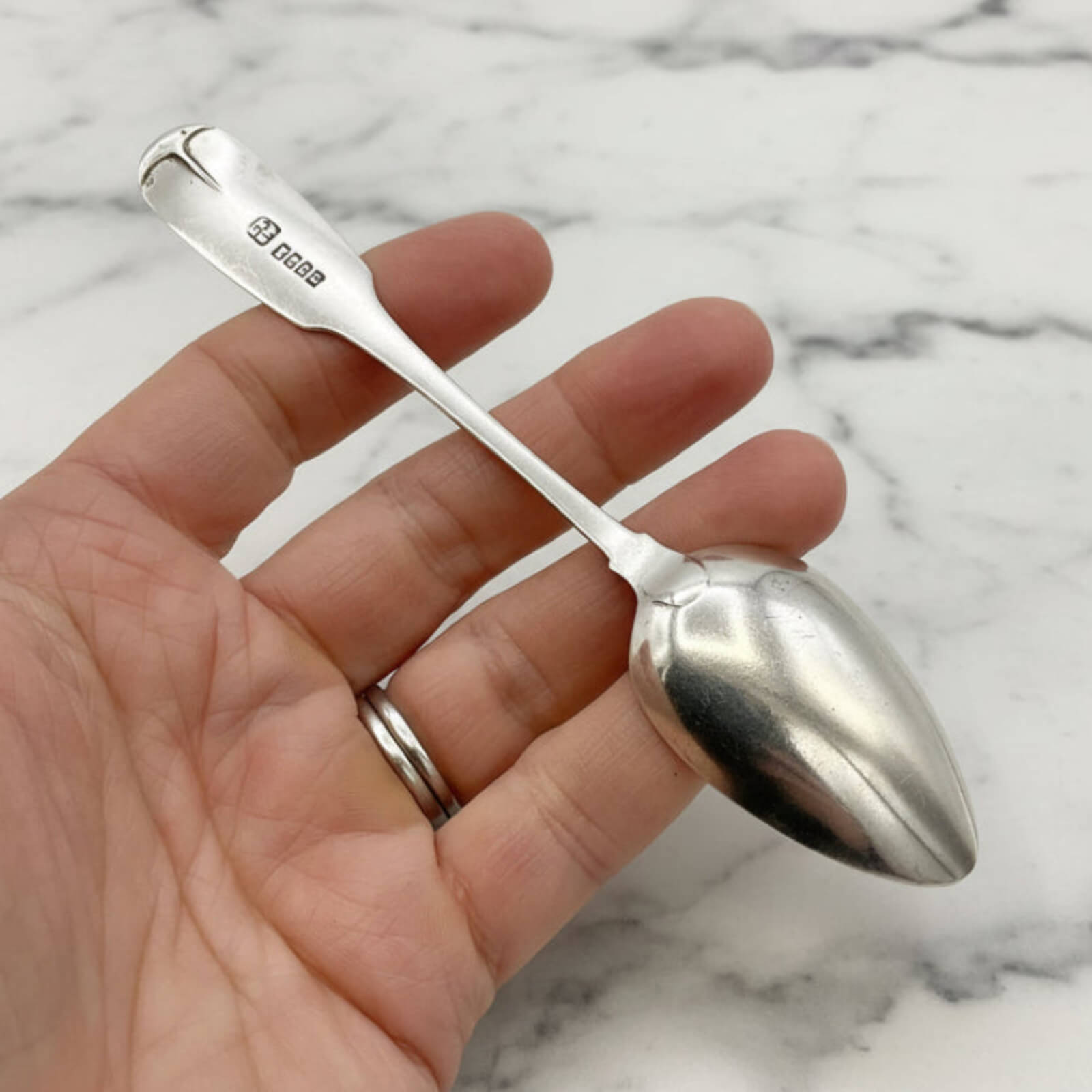Silver spoon held in a hand against a marble background