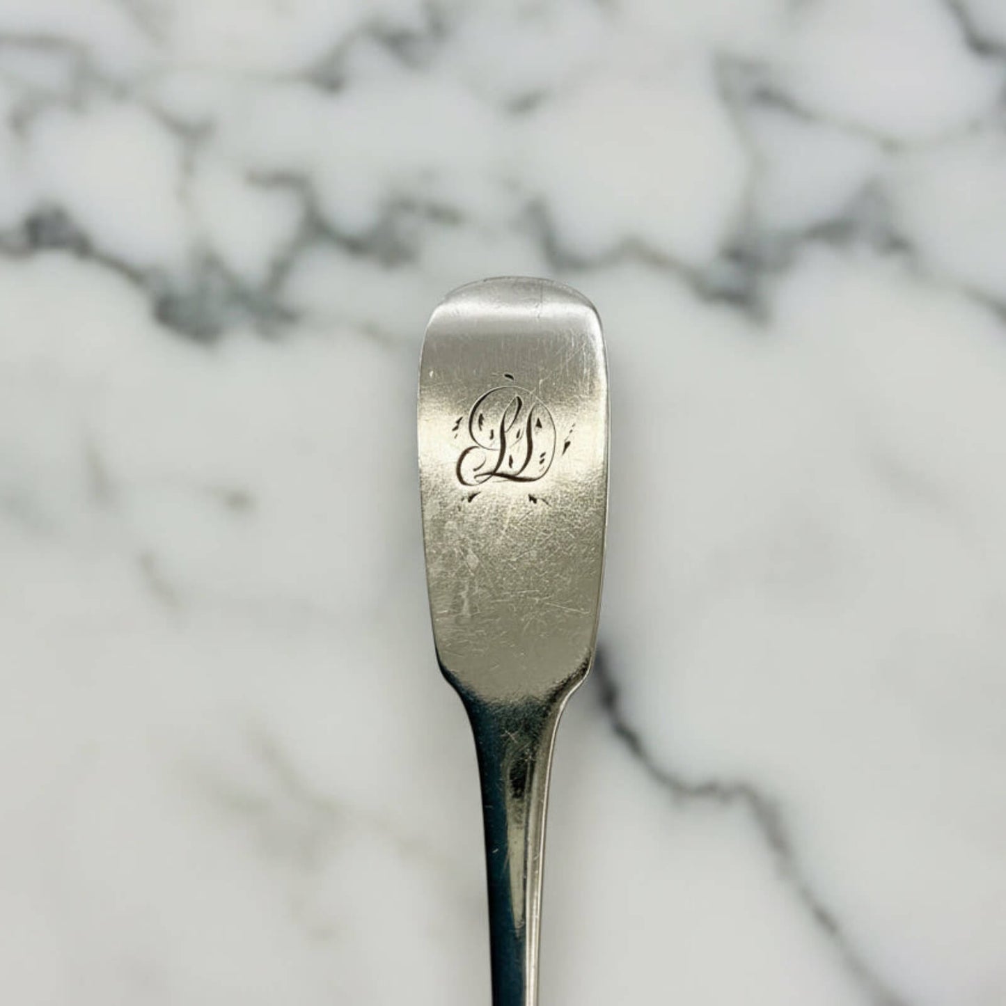 Silver spoon with engraved initials on a marble background