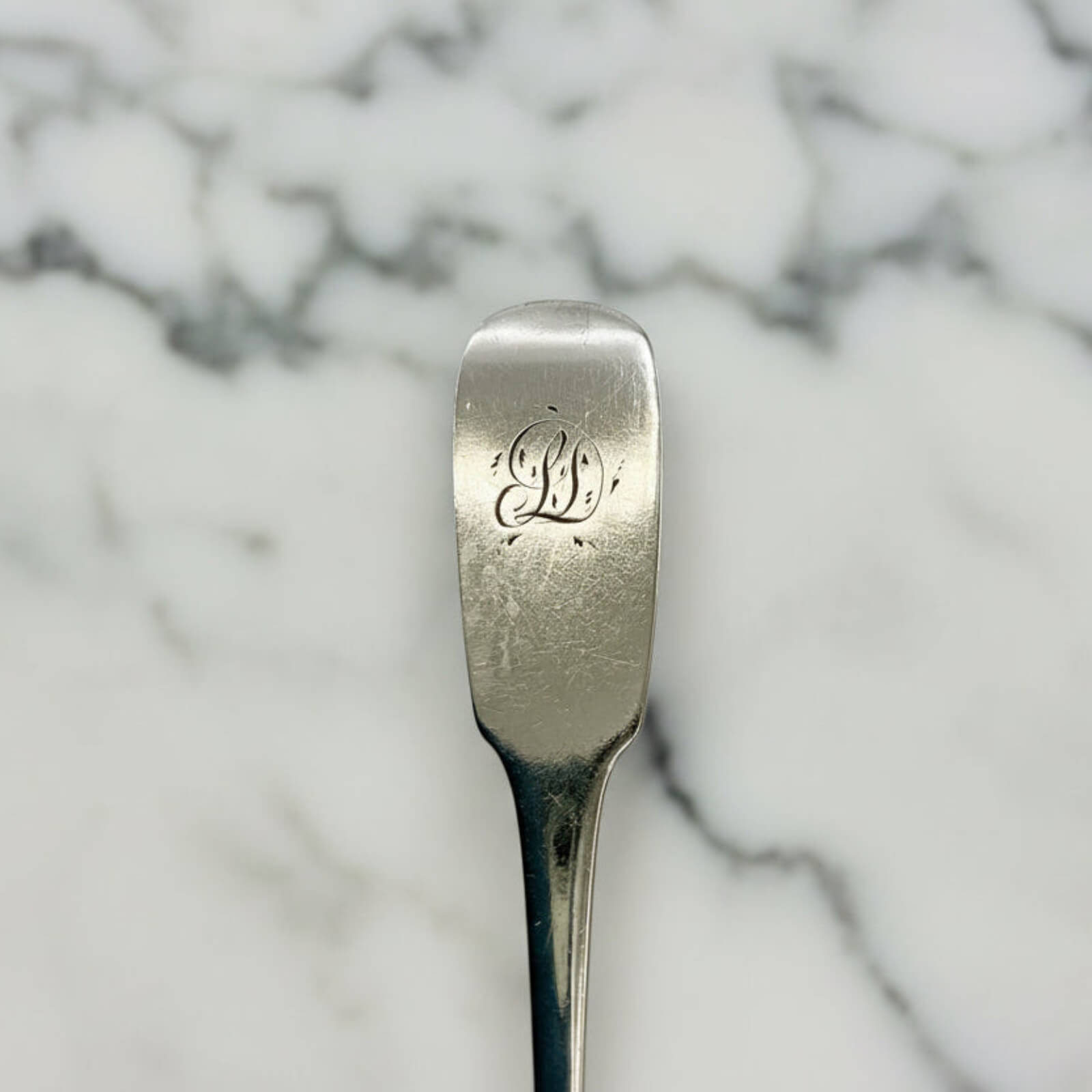 Silver spoon with engraved initials on a marble background