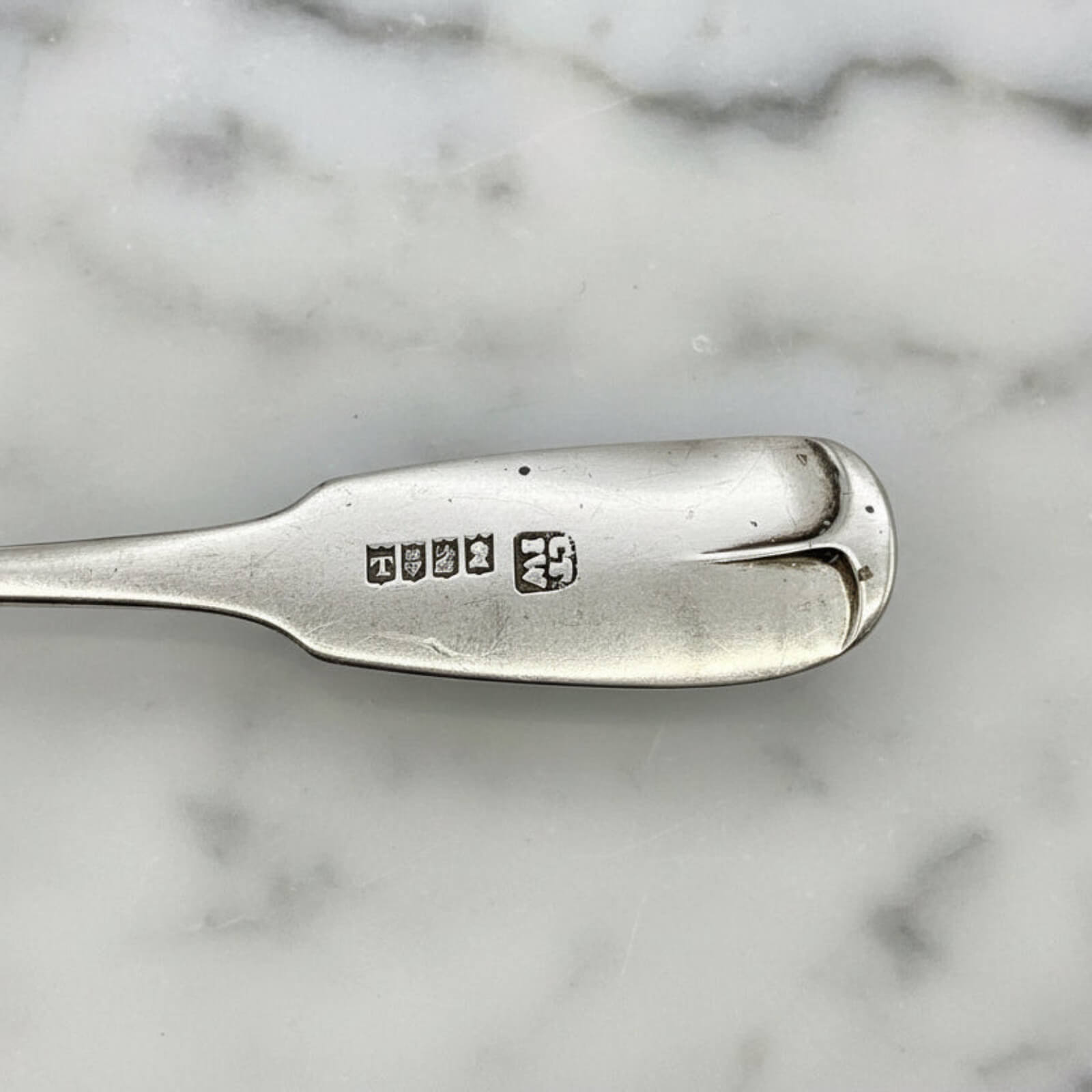 Silver spoon handle with engraved hallmarks on a marble background