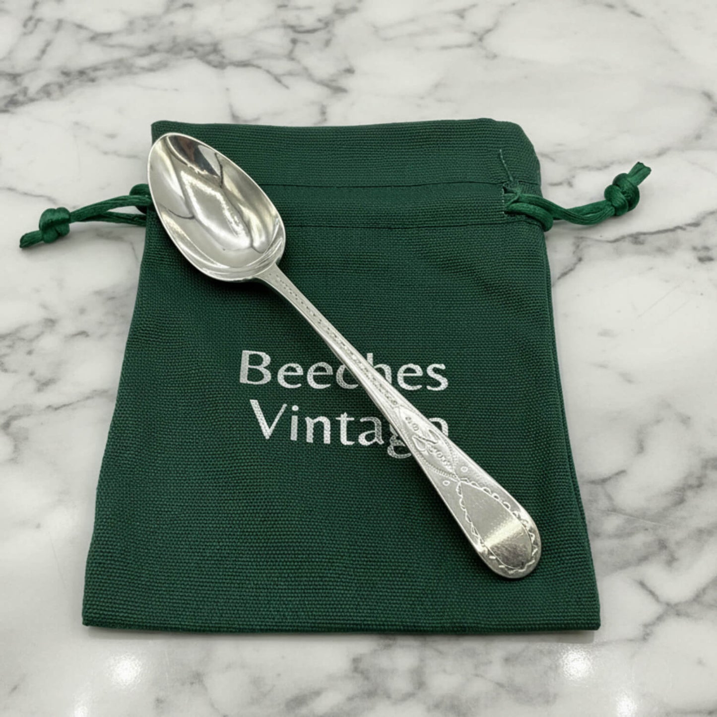 Silver spoon on a green drawstring bag with 'Beeches Vintage' text on a marble surface
