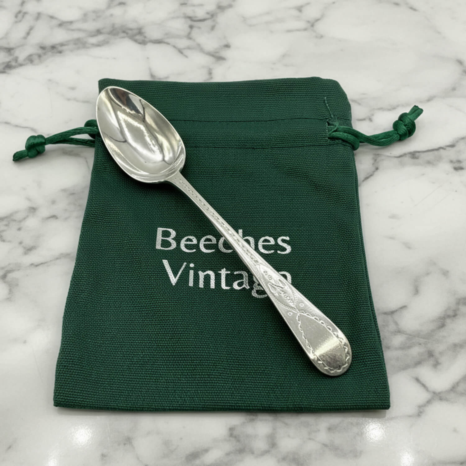 Silver spoon on a green drawstring bag with 'Beeches Vintage' text on a marble surface