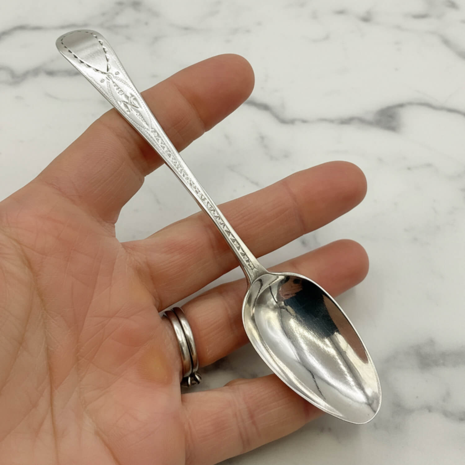 Silver spoon held in a hand against a marble background