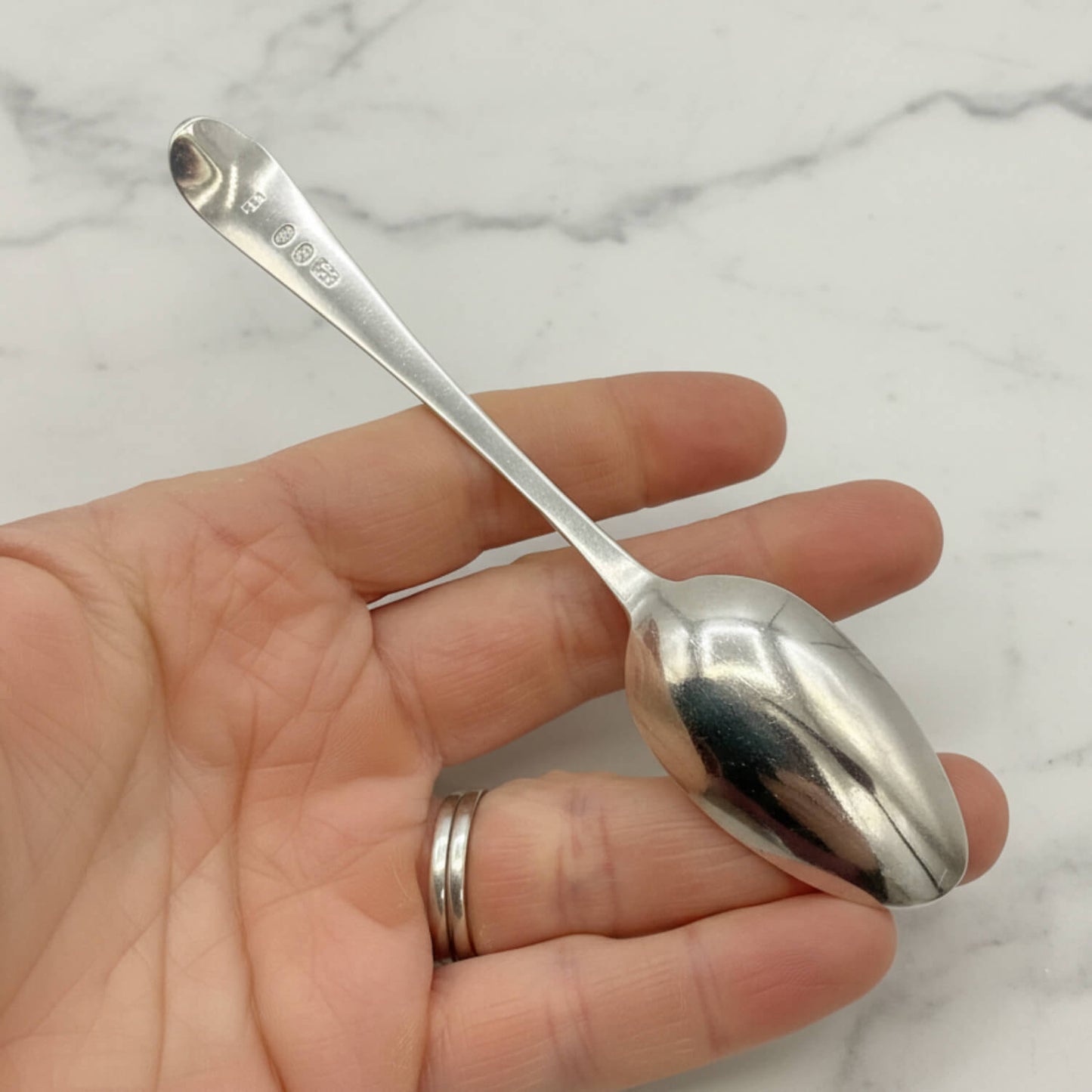 Silver spoon held in a hand against a marble background