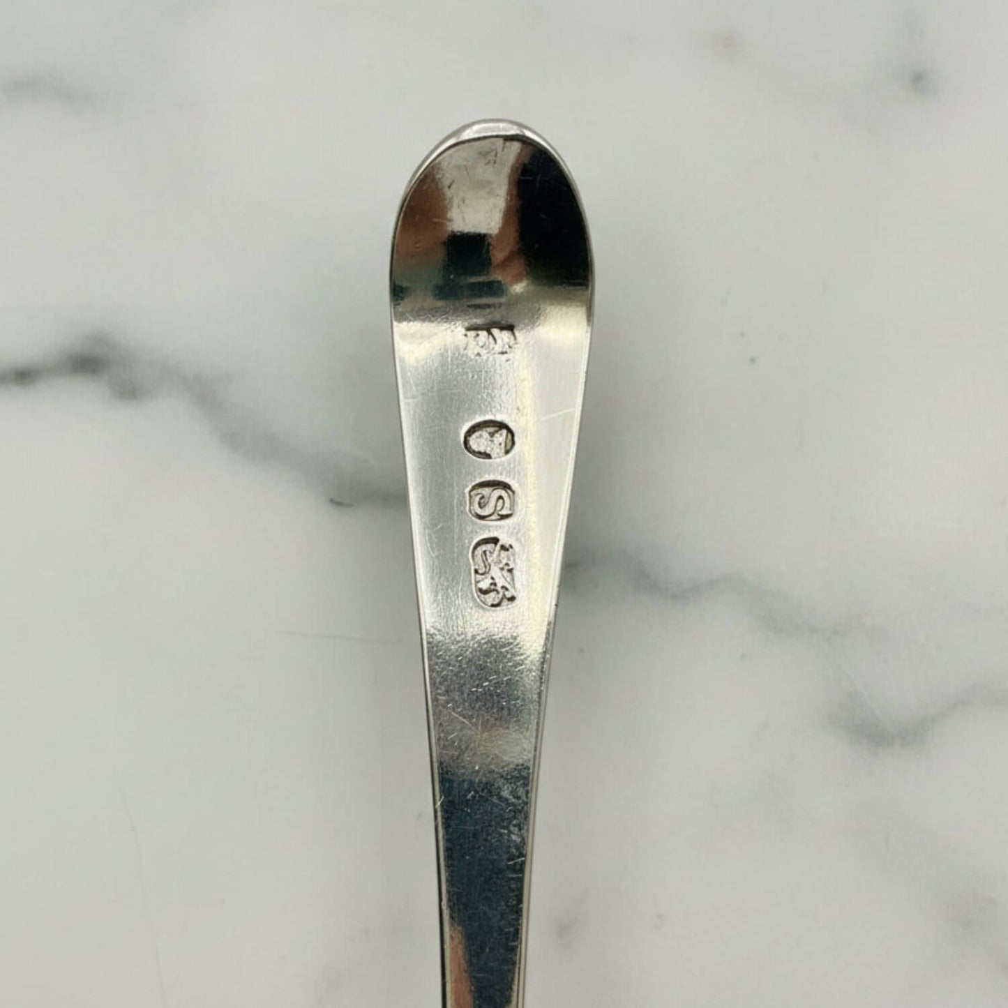 Antique Georgian Sterling Silver Teaspoon, Hallmarked 1793 showing the hallmarks against a marble surface