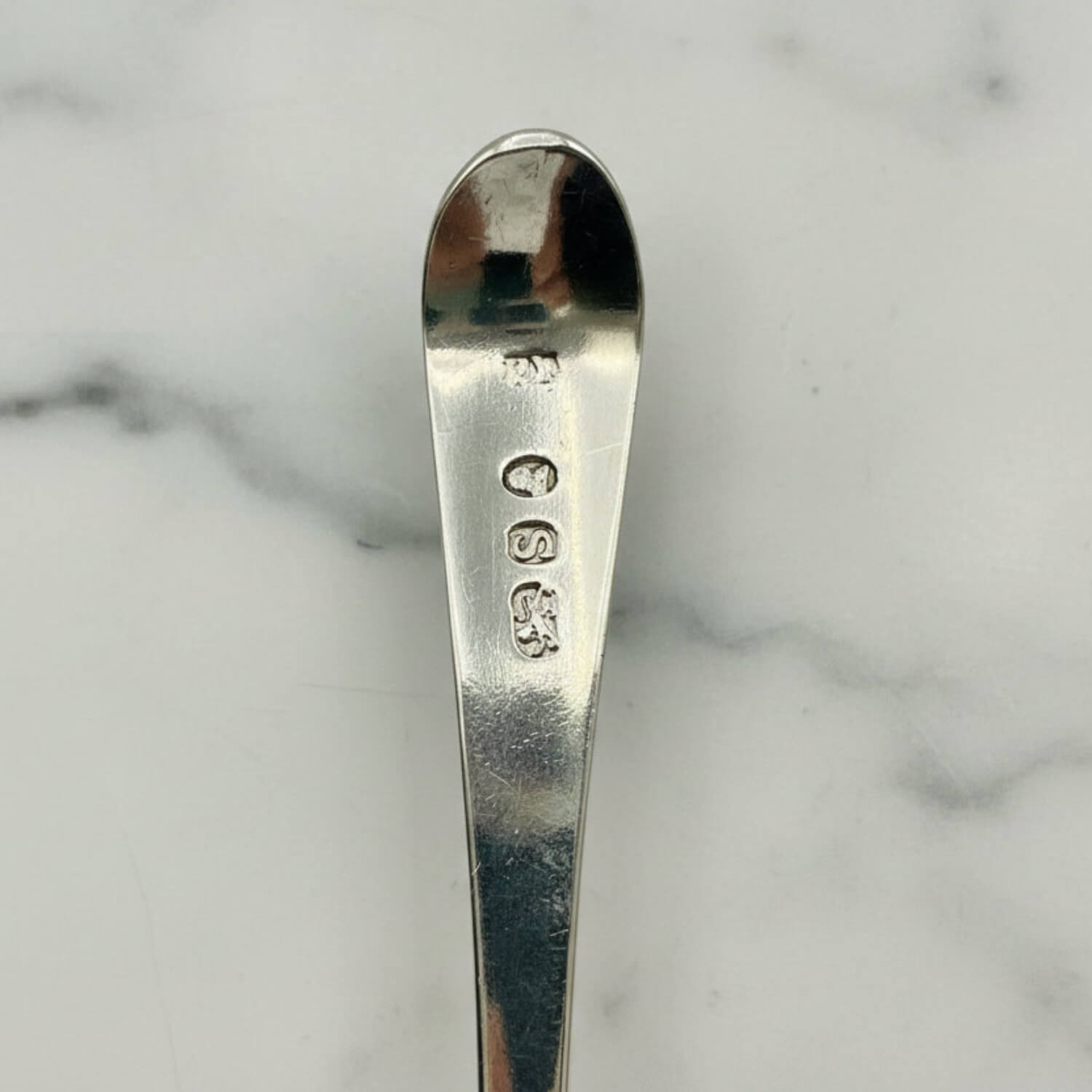 Antique Georgian Sterling Silver Teaspoon, Hallmarked 1793 showing the hallmarks against a marble surface
