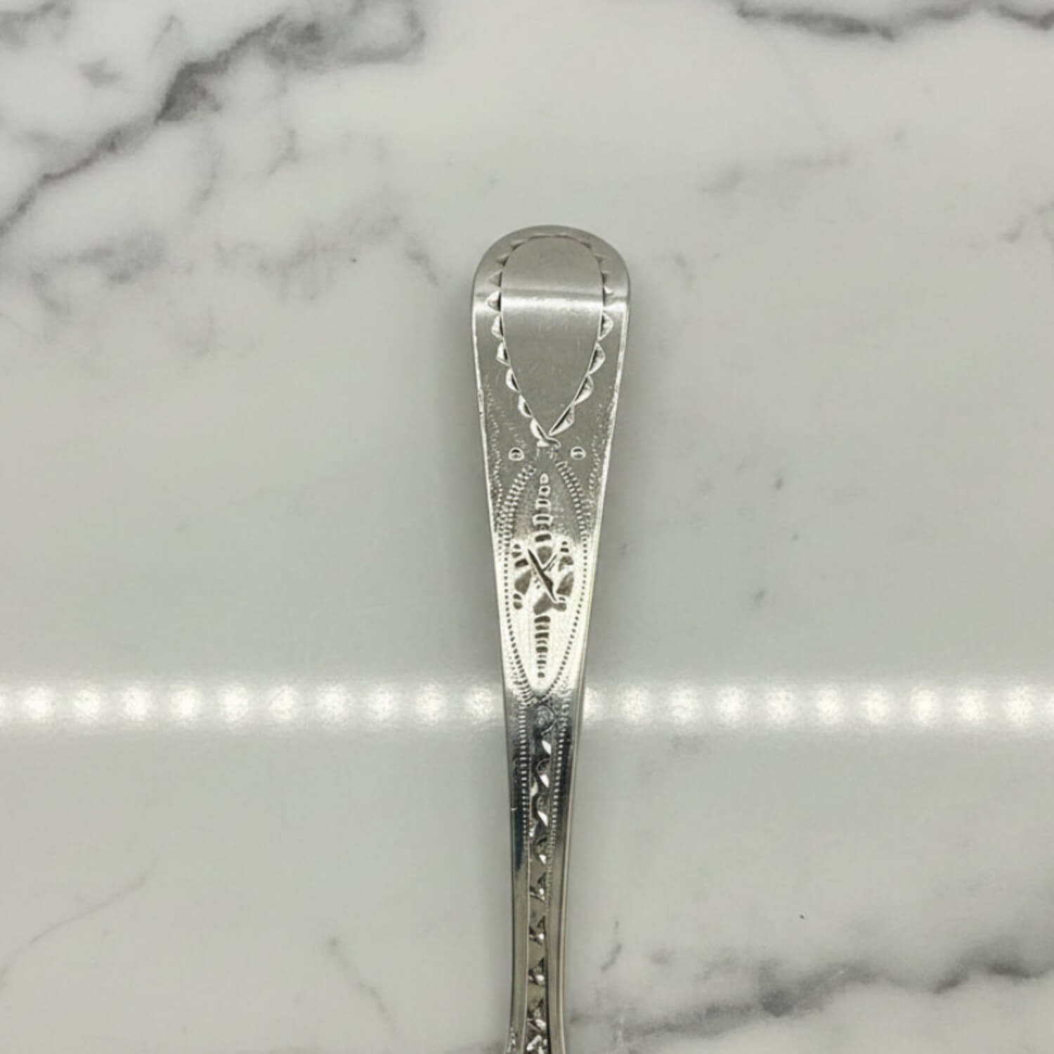 Silver spoon with intricate design on a marble surface