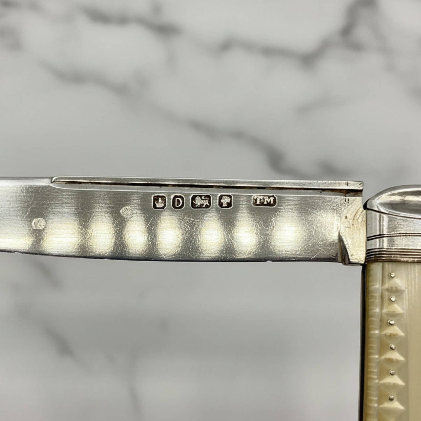 Close-up of a silver fruit knife with engraved details on a marble surface