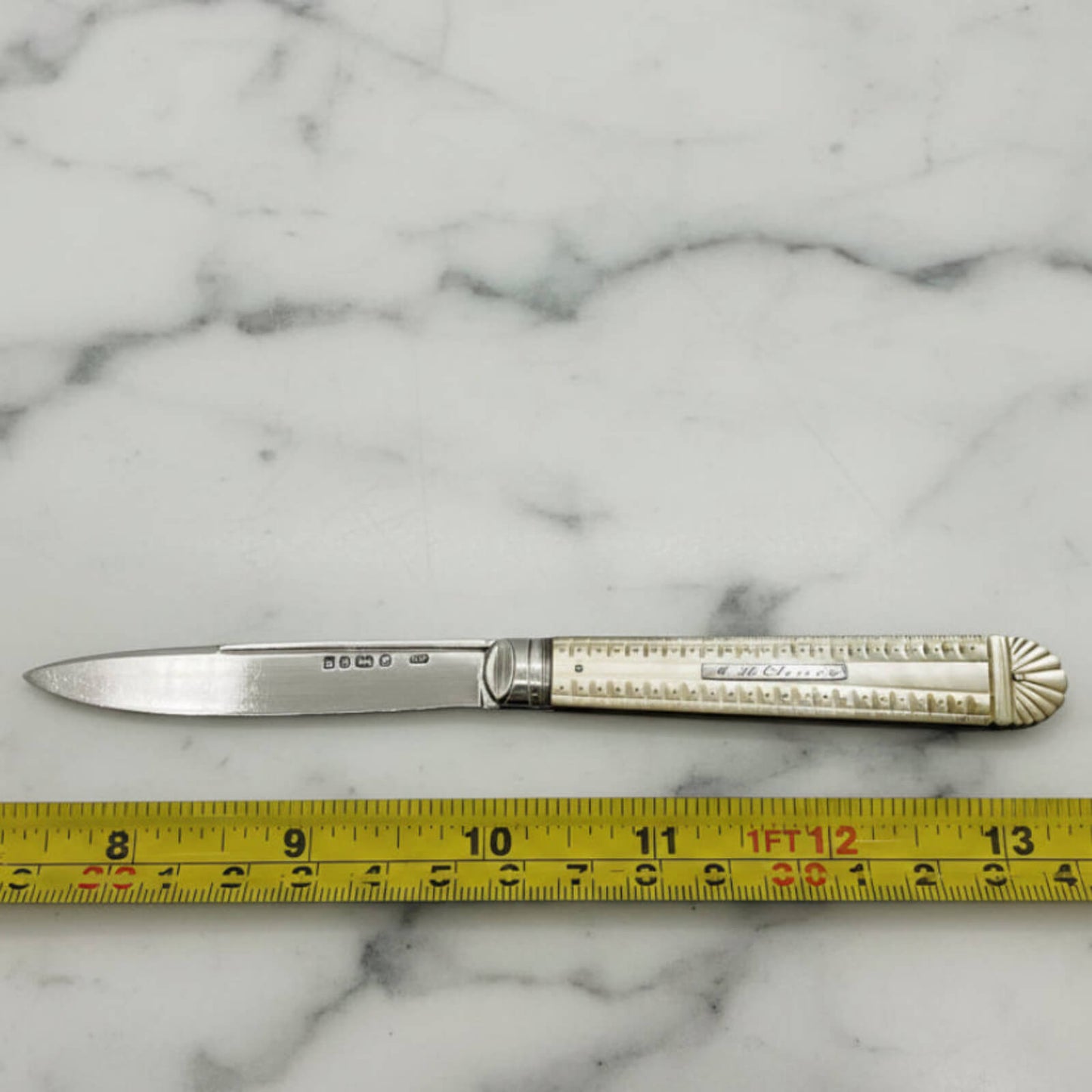 Decorative knife with ornate handle on a marble surface, measured by a ruler.